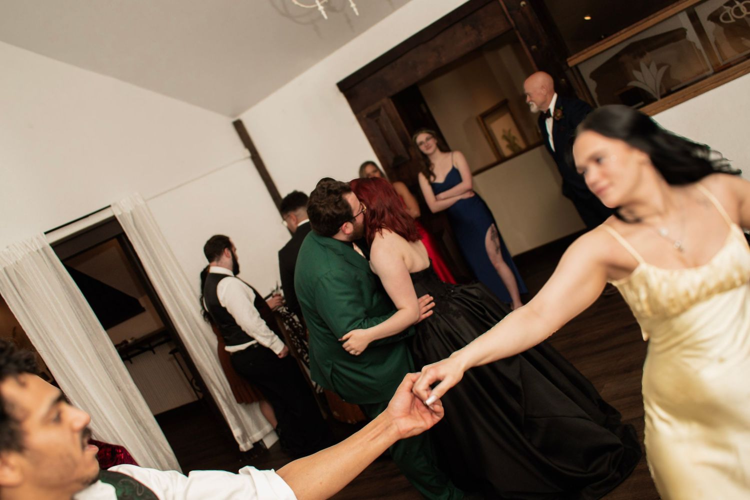 Wedding guests dancing energetically at elegant indoor reception with string lights and formal attire.