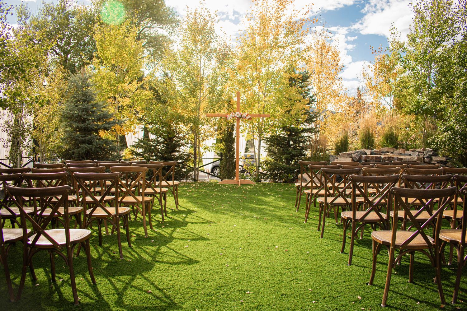 Elegant outdoor wedding ceremony,  with wooden chairs on a lawn surrounded by autumn trees, at Hearth House Wedding Venue in Monument, CO