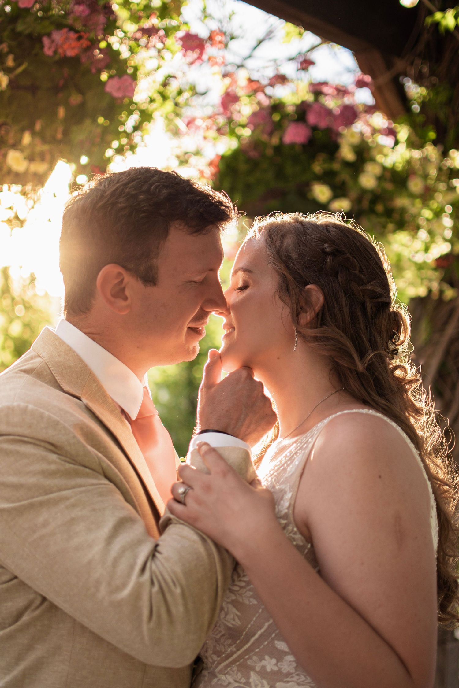 Bride and groom sharing a romantic moment under floral arch in golden sunset light at outdoor wedding.