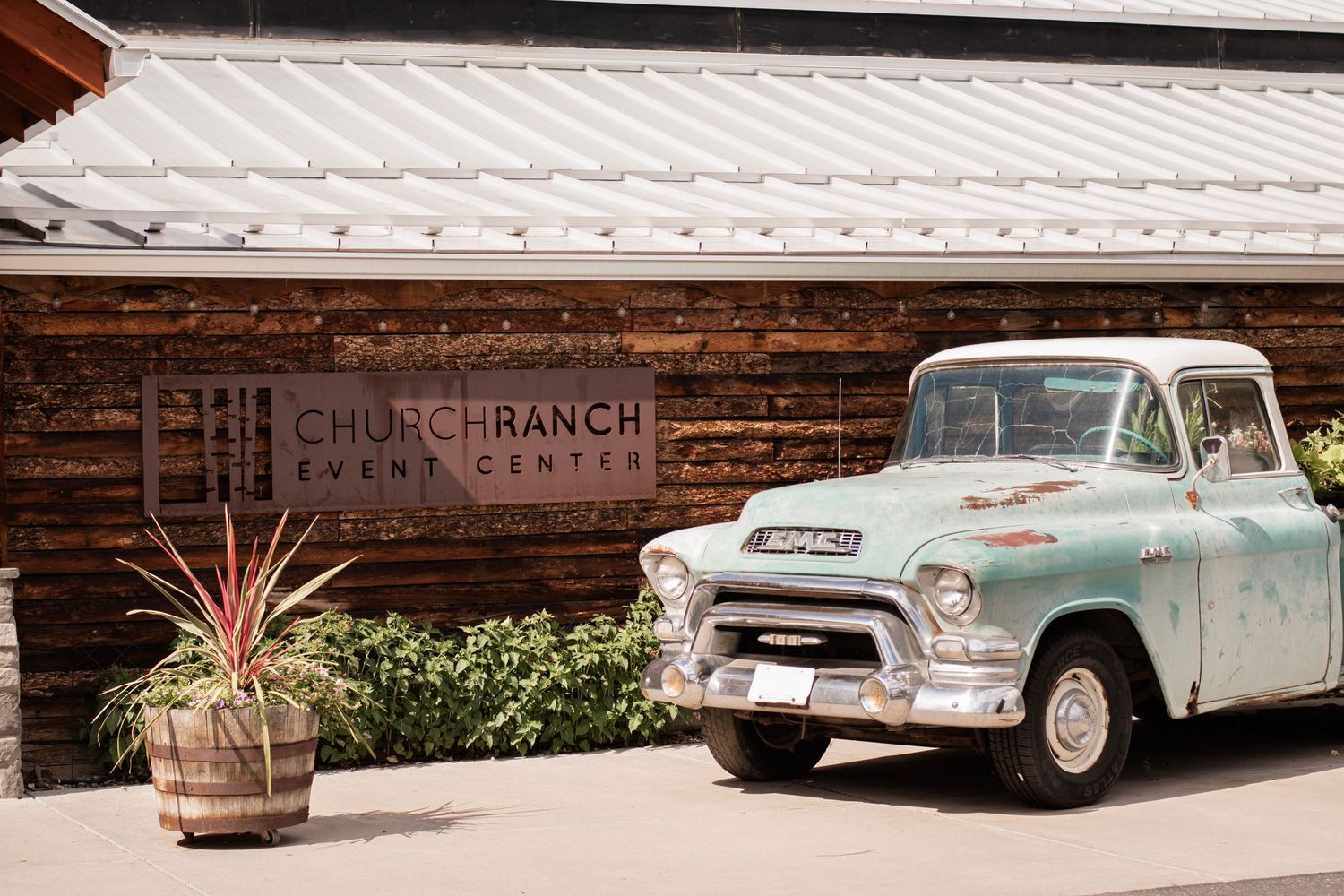 Vintage turquoise GMC pickup truck parked outside Church Ranch Event Center in Westminster, CO with wood facade and modern signage.