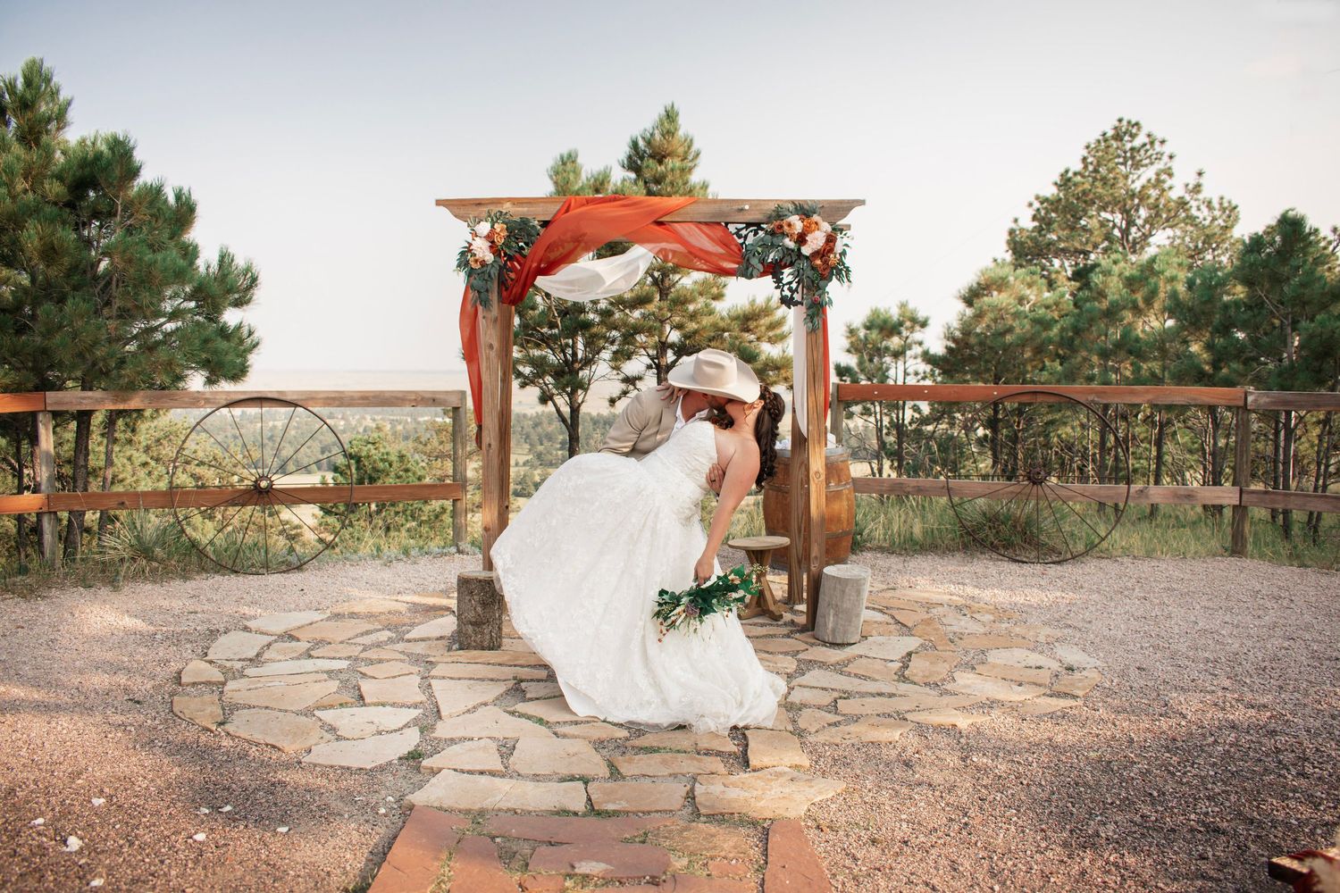 Bride in white gown standing under rustic wooden arch with red floral decor at outdoor wedding ceremony at Once Upon Events