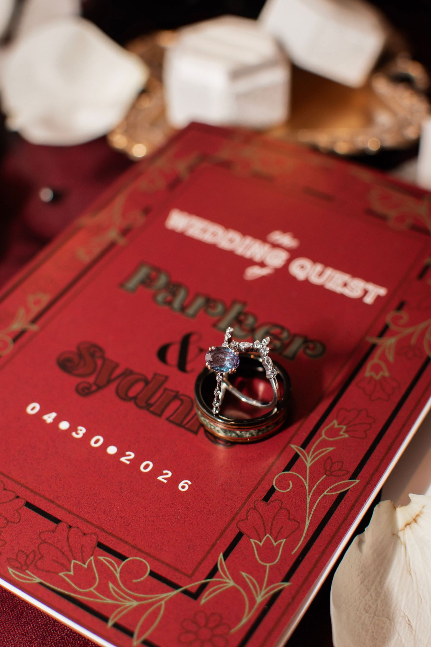 Red wedding invitation card for Parker and Sydney dated 04.30.2026 with elegant rings resting on top.