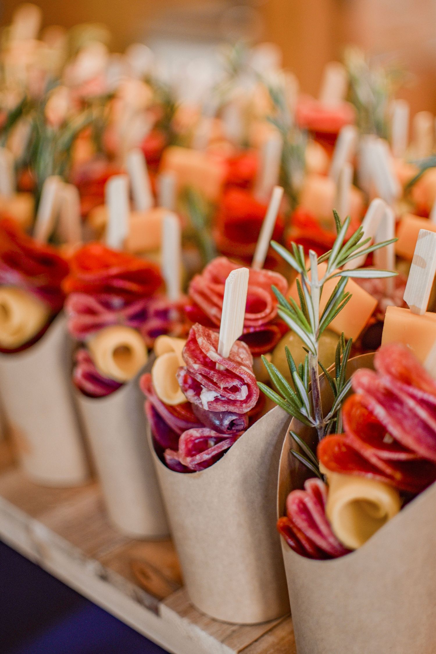 Elegant charcuterie cones filled with salami, cheese, and rosemary sprigs arranged on a wooden tray for catering.