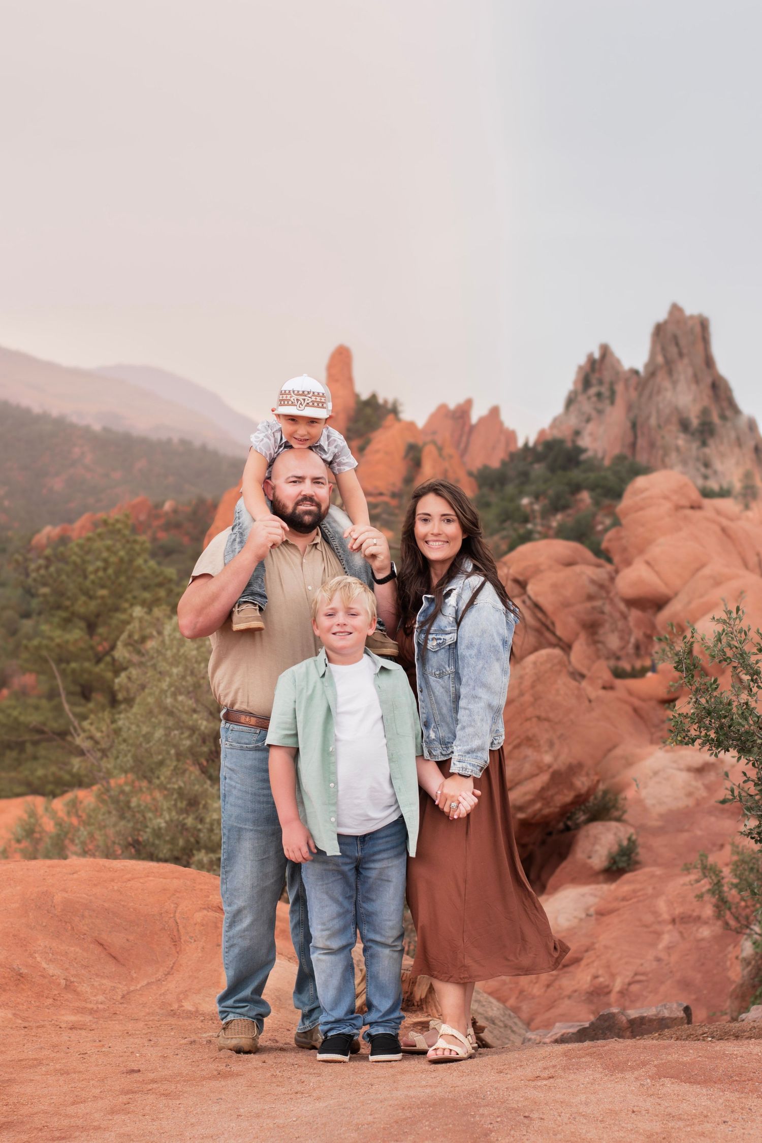 Family of four posing at Garden of the Gods, Colorado, with red rock formations in the background.