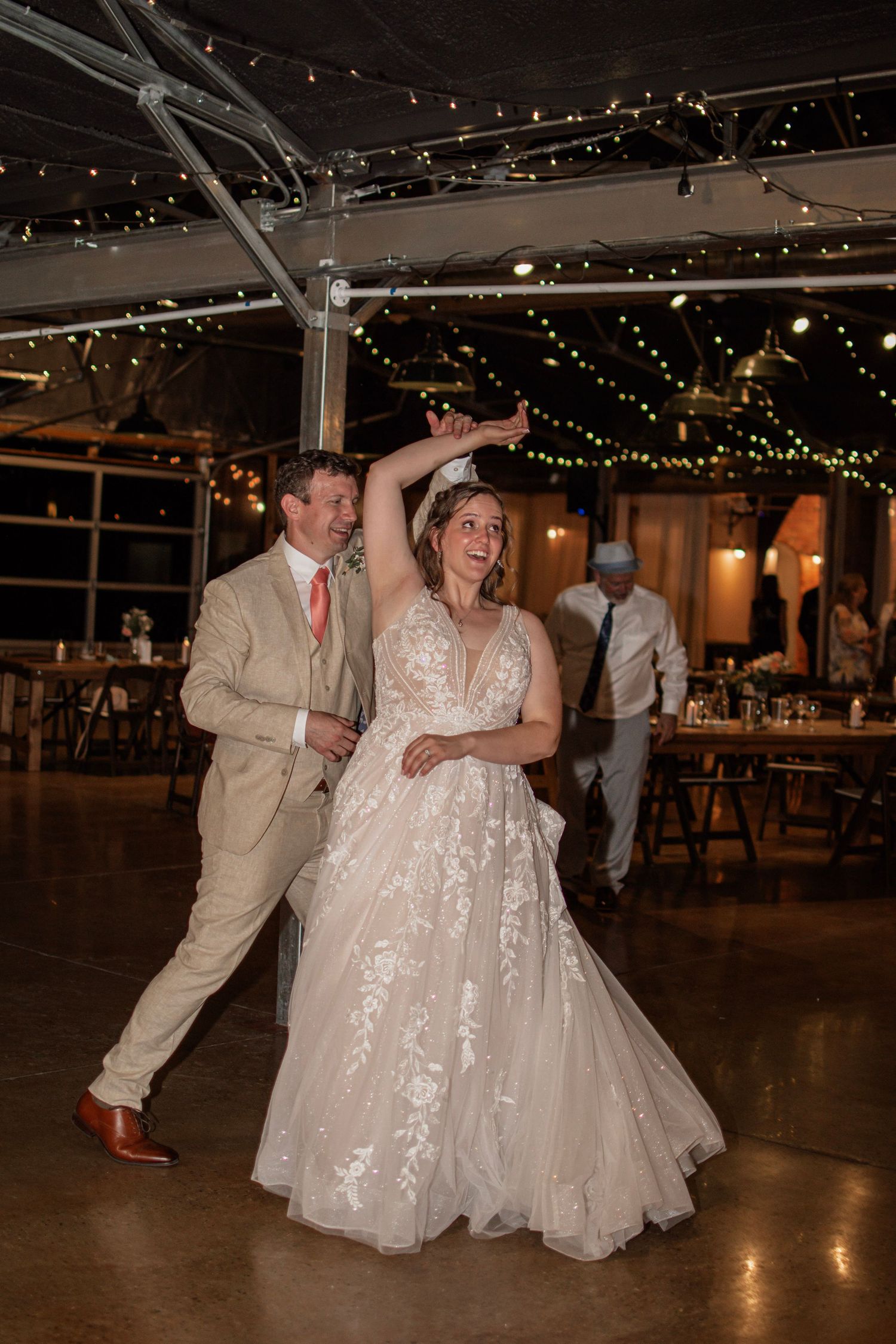 Bride and groom sharing first dance under twinkling string lights at rustic wedding reception.