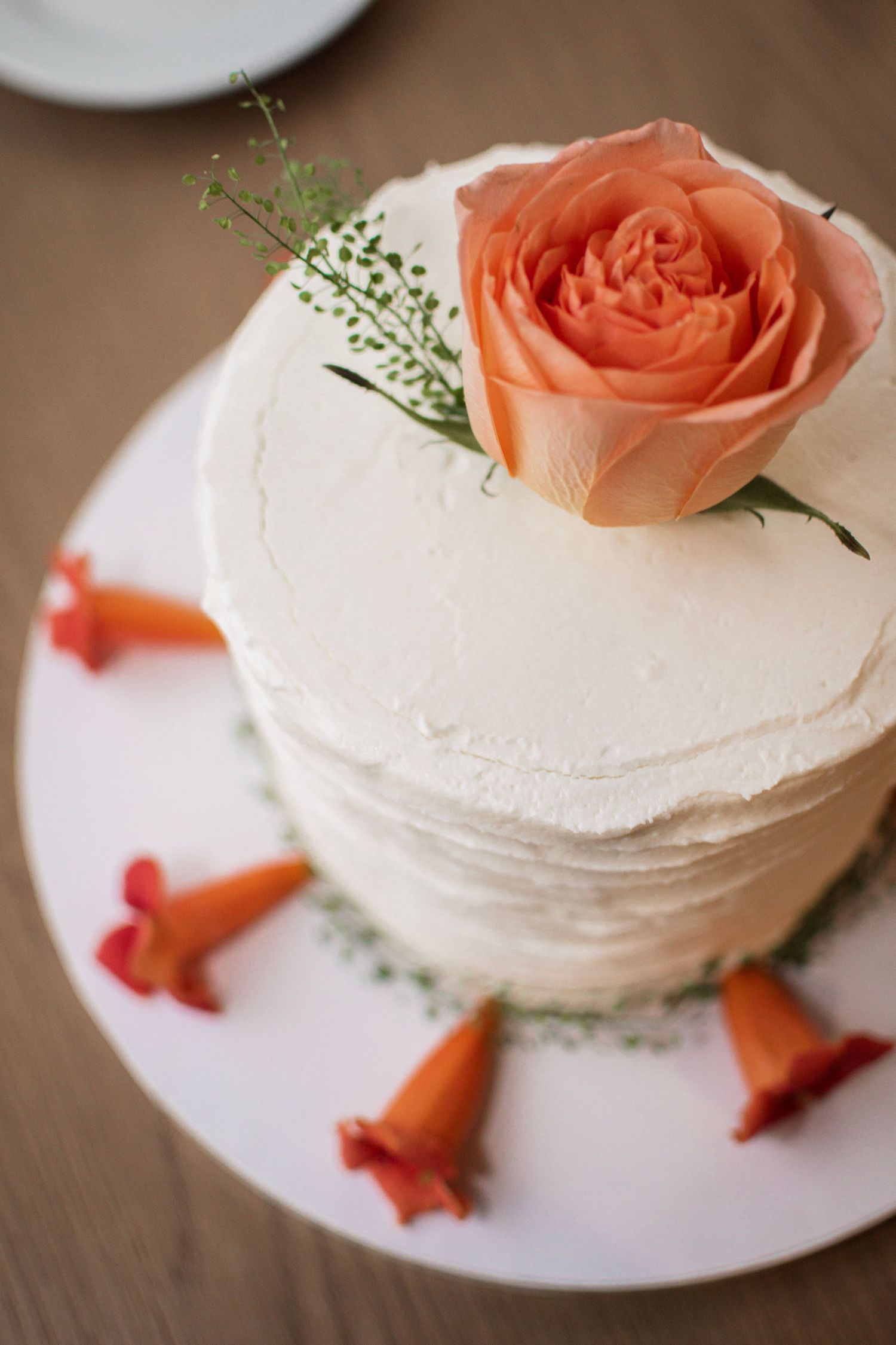 Elegant single-tier white wedding cake topped with a peach rose and orange floral accents.