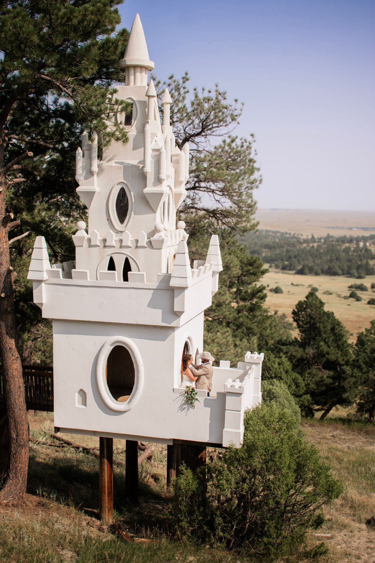 bride and groom on a white castle at Once Upon a Time Events, surrounded by pine trees with scenic rolling hills in the background.