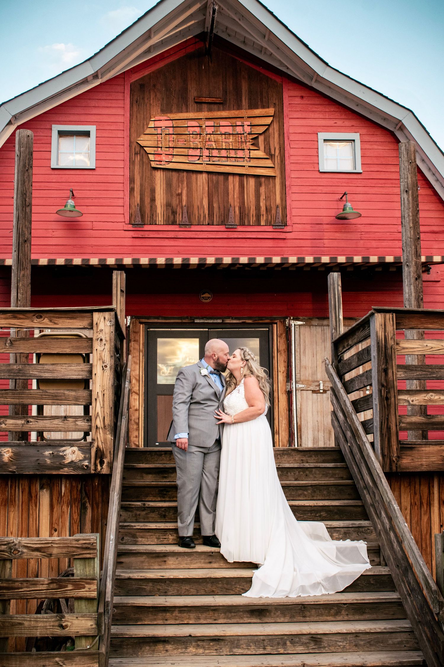 Bride and groom kissing on stairs of a rustic red D- barn wedding venue at dusk.