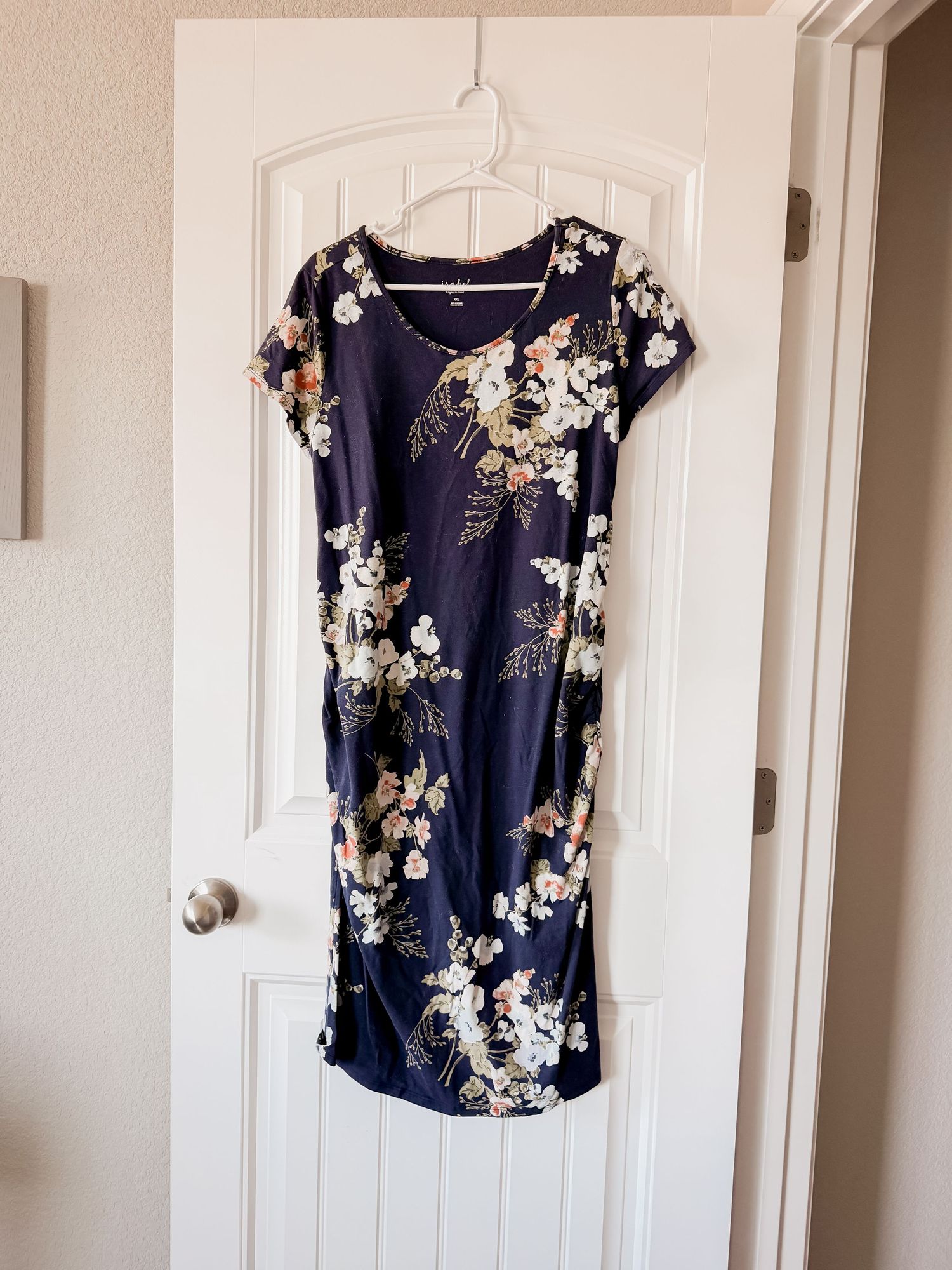 Navy blue floral short-sleeve dress with ruched sides and pink and white blossoms hanging on a white paneled door.