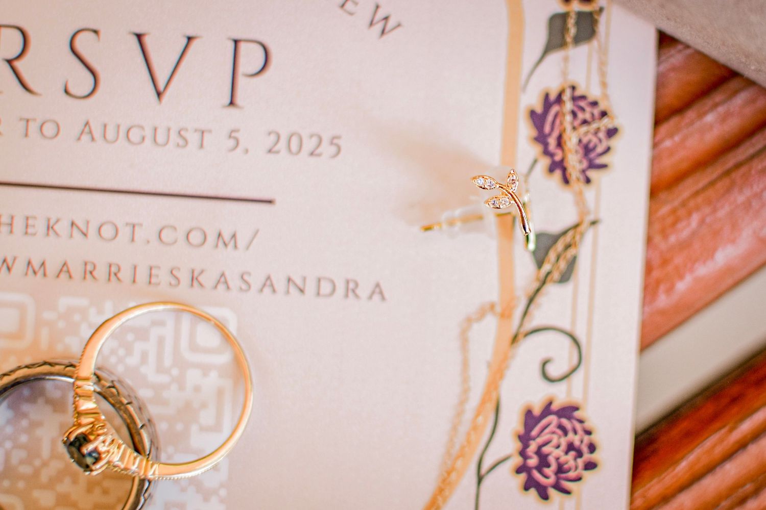 Gold wedding rings and a floral RSVP card for a 2025 wedding at theknot.com/marrieskasandra.