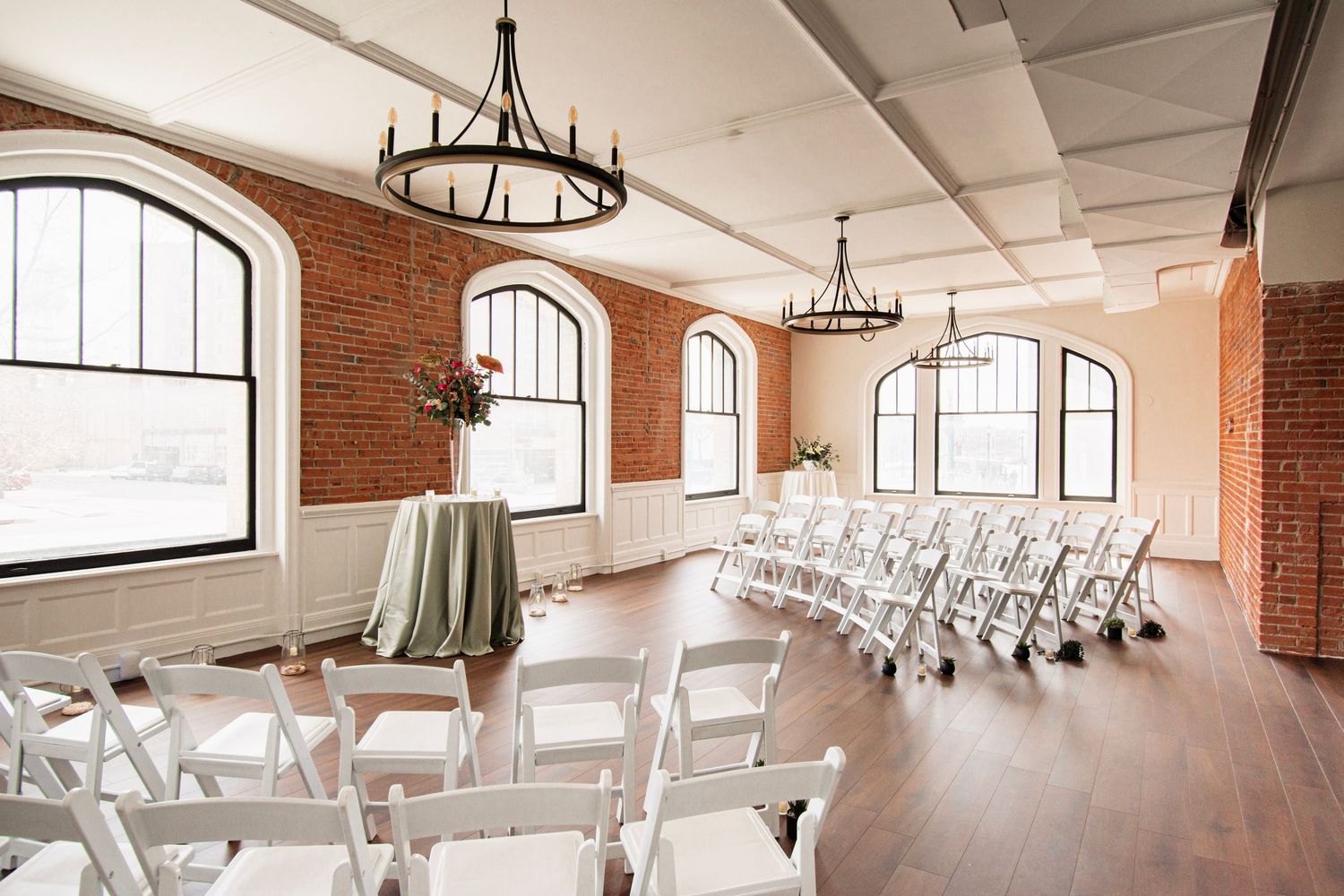 Elegant wedding venue Loft 130 in Colorado Springs, CO with brick walls, arched windows, and wrought iron chandeliers on hardwood floors.