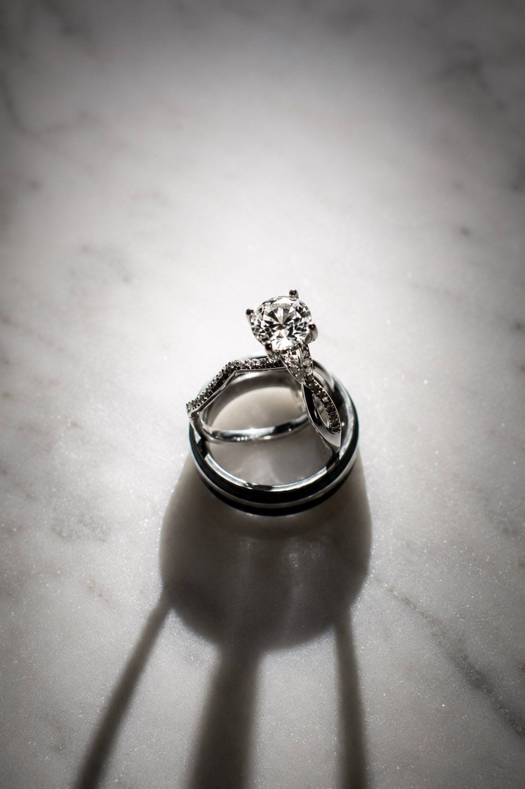 Diamond engagement ring and wedding band set displayed on marble surface with dramatic shadow.