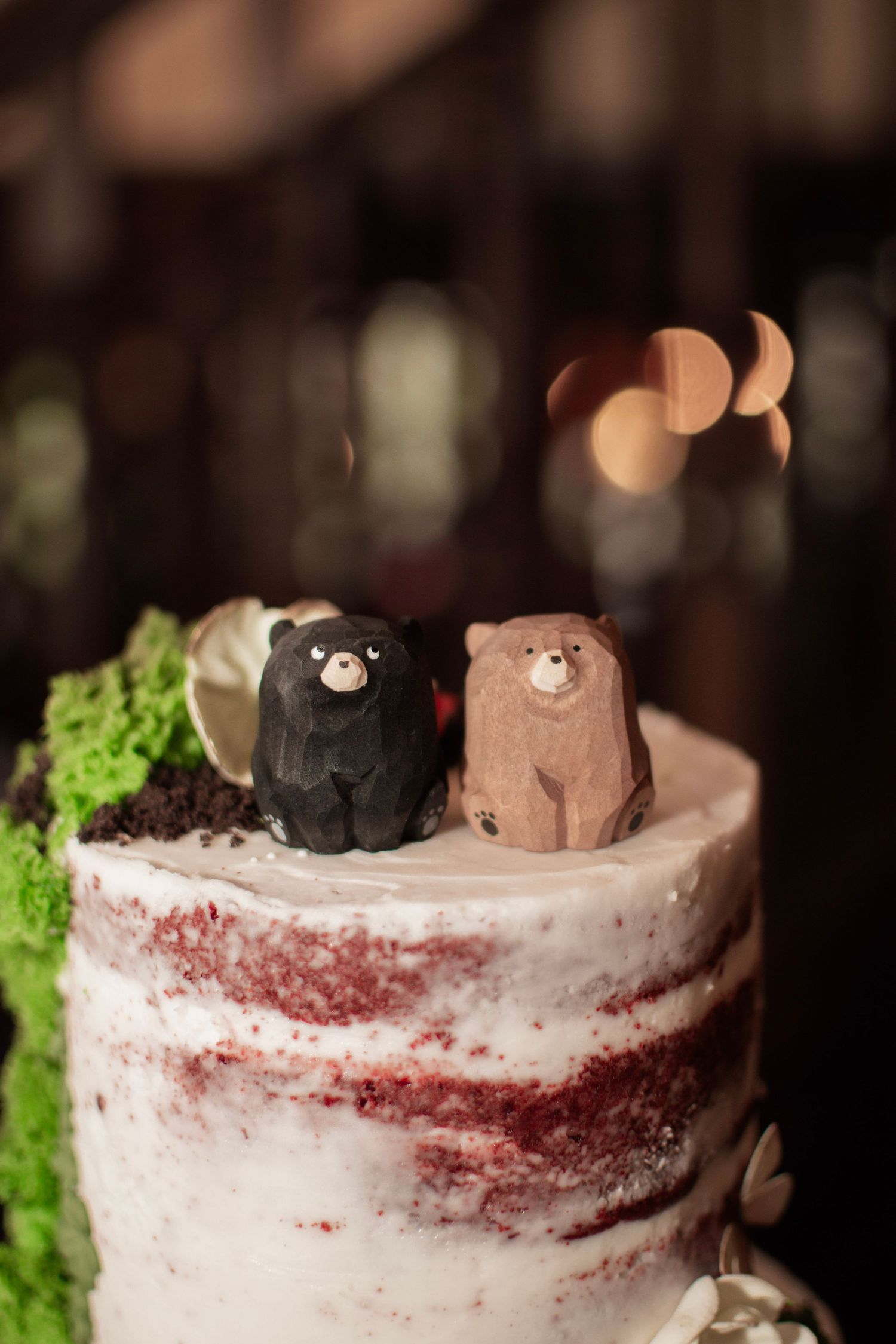 Two bear cake toppers on a rustic naked red velvet wedding cake decorated with green moss.