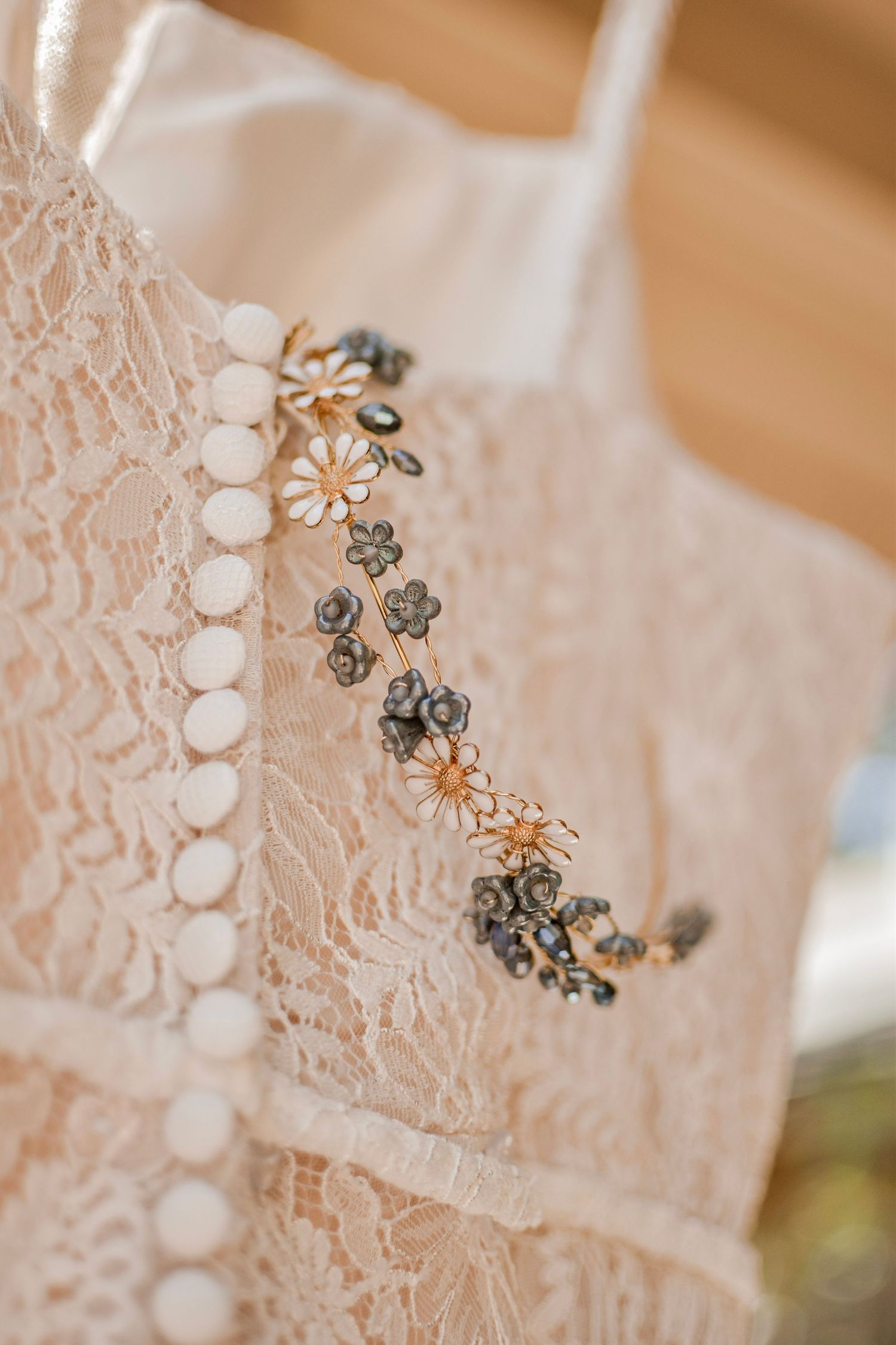 Close-up of a lace wedding dress with pearl buttons and a delicate floral gold hair vine accessory.