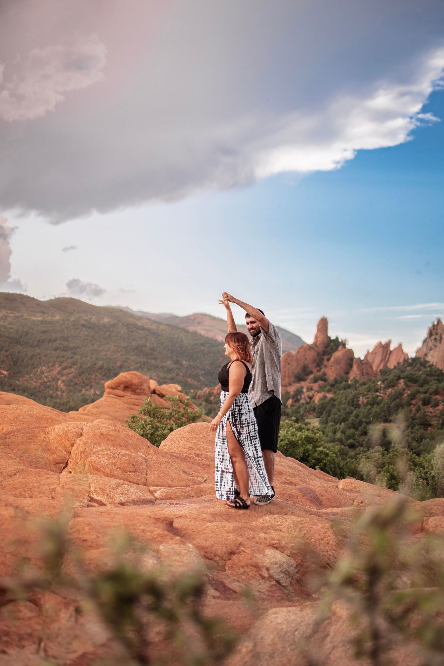 Couple dancing on red rocks at Garden of the Gods, Colorado, with dramatic mountain views and cloudy blue sky.