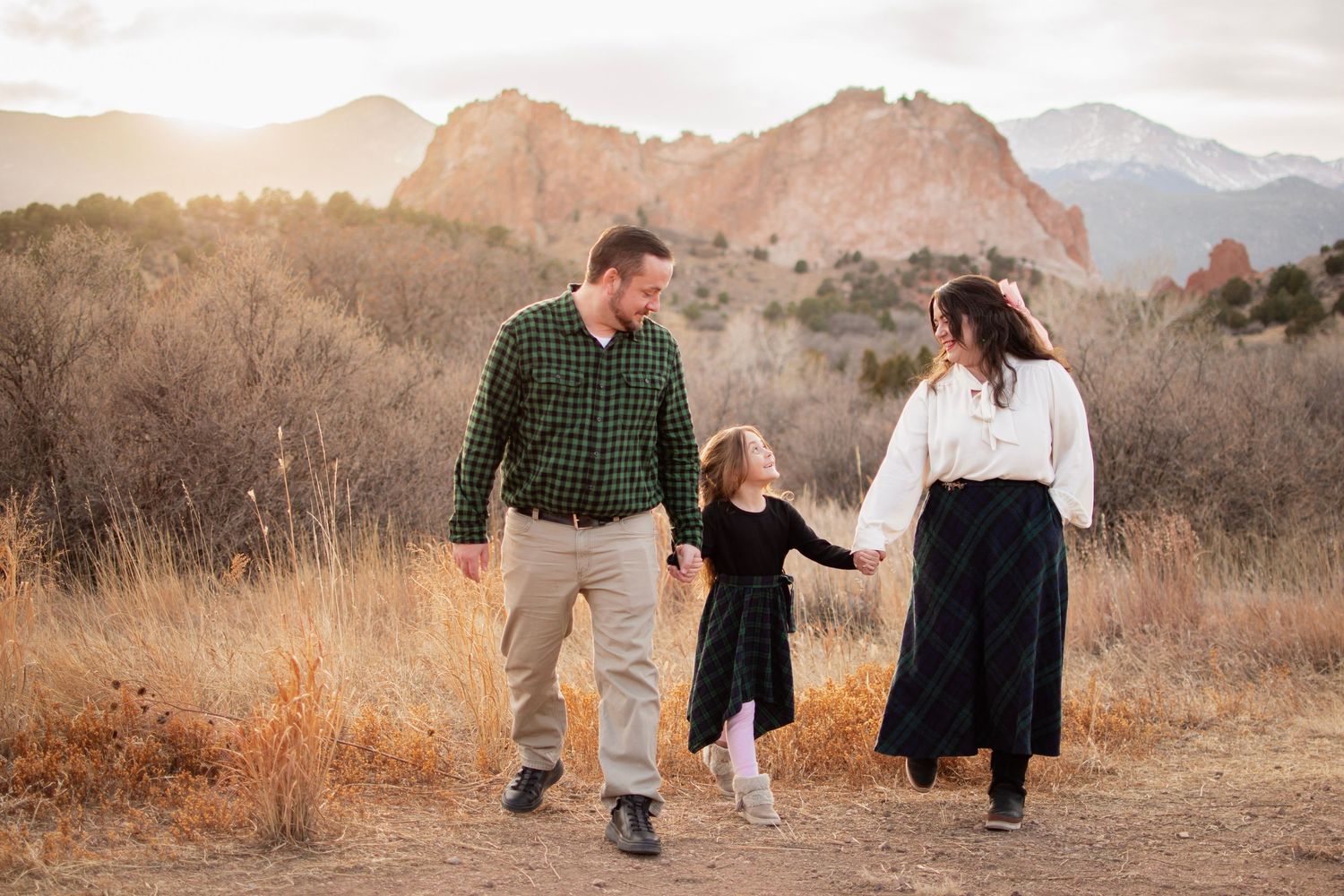 Family of three walking hand-in-hand on a mountain trail at Garden of the Gods, Colorado, at golden hour.