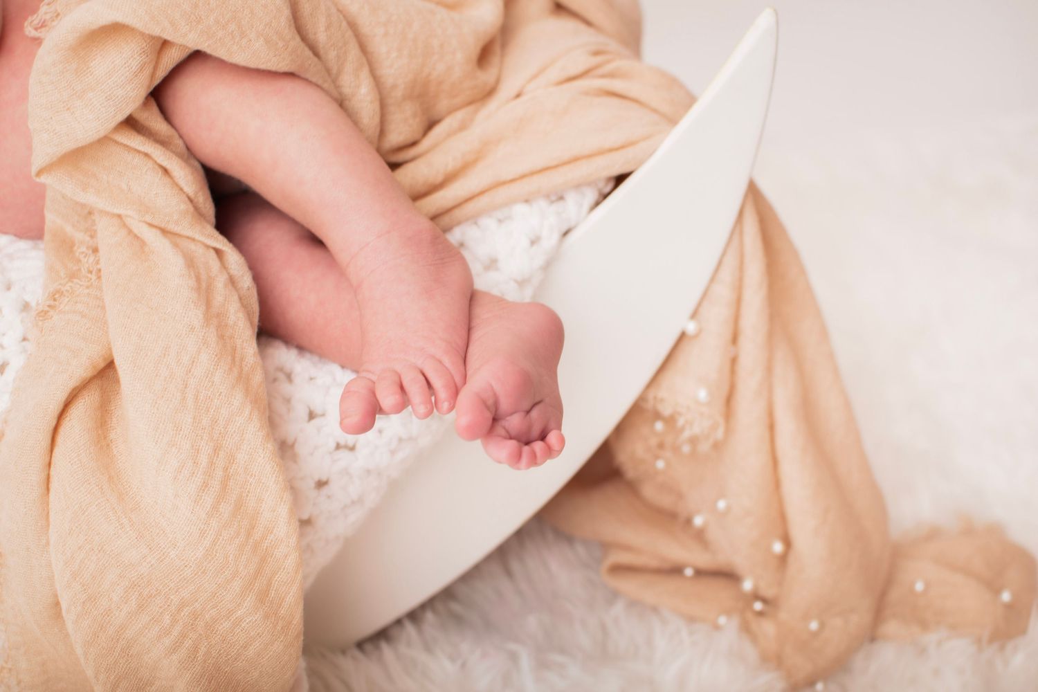 Close-up of tiny newborn baby feet resting in a white bowl, wrapped in a soft beige muslin blanket at Luminous Creative Studios.