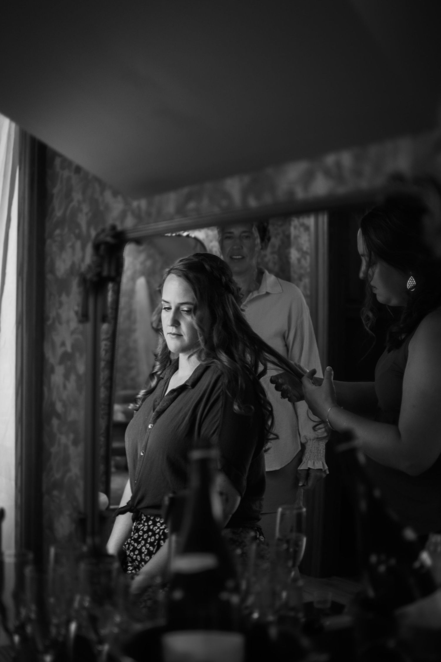 Black and white photo of bride getting hair styled by attendant before wedding ceremony.