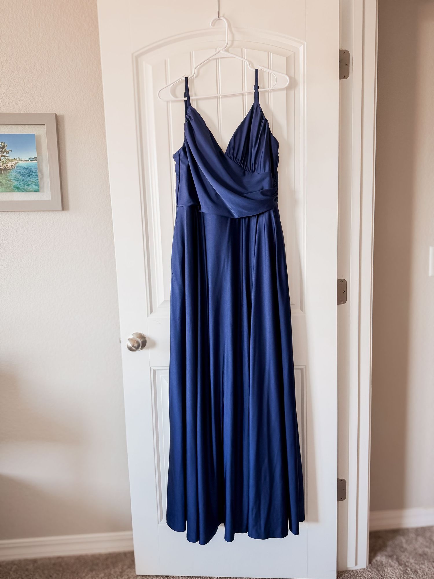 Navy blue floor-length bridesmaid dress with spaghetti straps and a draped V-neckline hanging on a white paneled door.