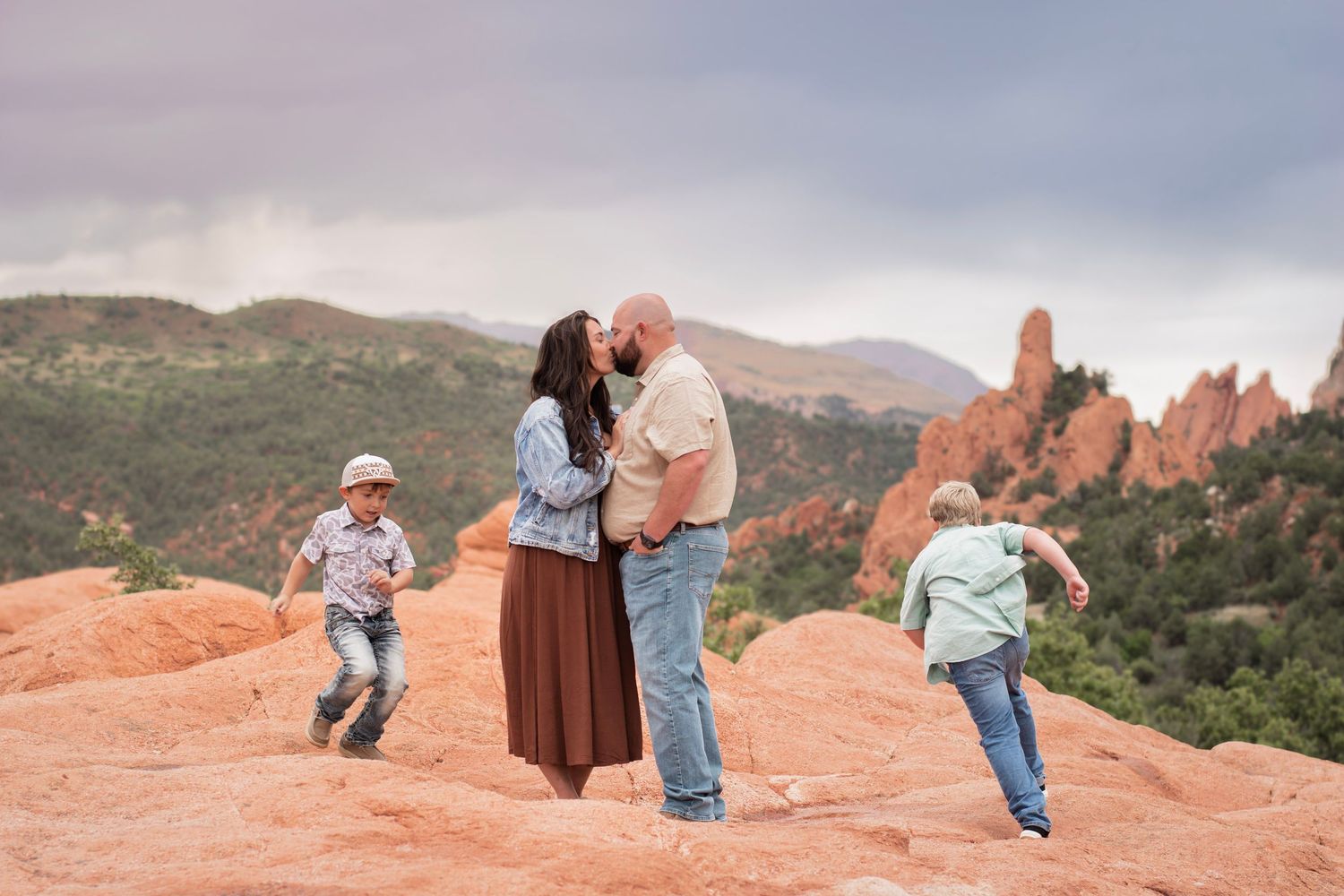 Family kissing on red rocks at Garden of the Gods, Colorado, with two children playing around them.