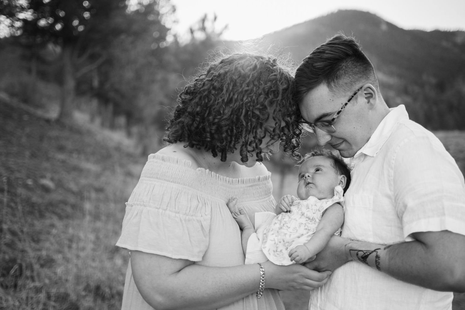Black and white photo of parents tenderly holding their newborn baby outdoors with mountains in the background.