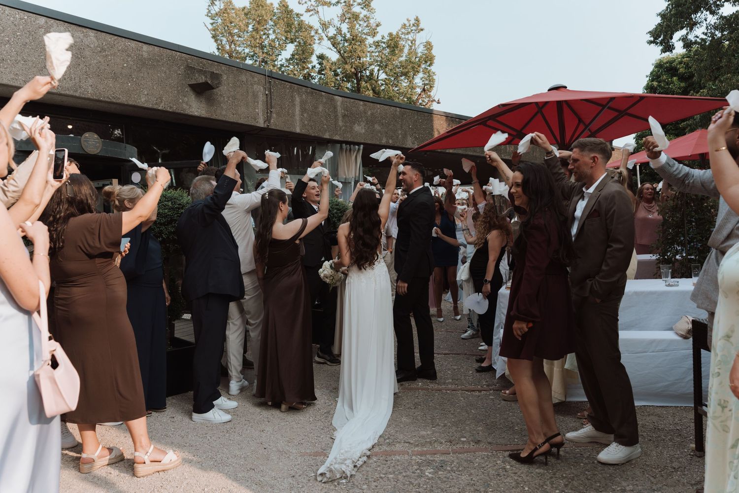 Bride and groom walking through a celebratory send-off line of cheering wedding guests outdoors.