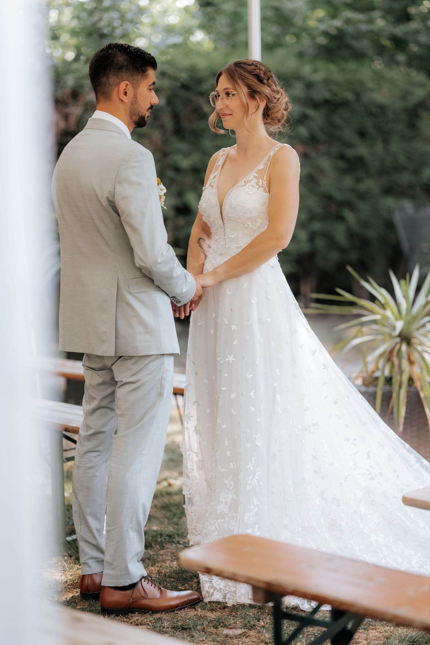 Bride and groom holding hands during outdoor wedding ceremony surrounded by lush greenery.