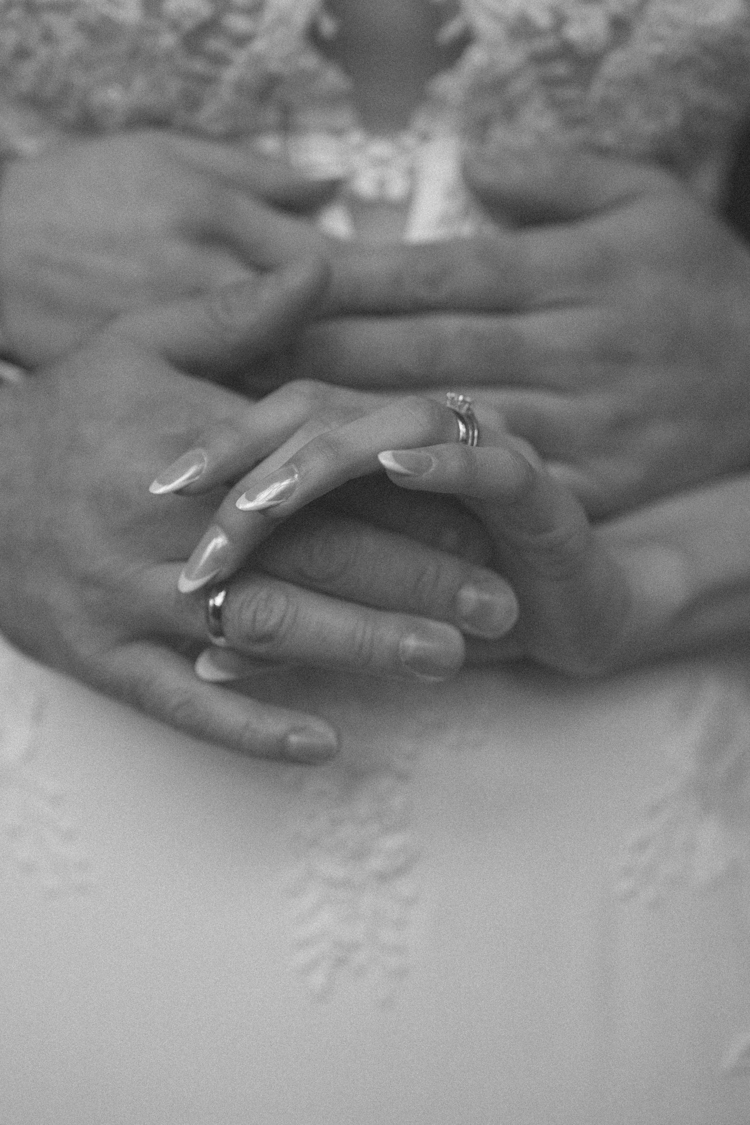 Black and white photo of bride and groom's hands clasped together showing wedding rings.