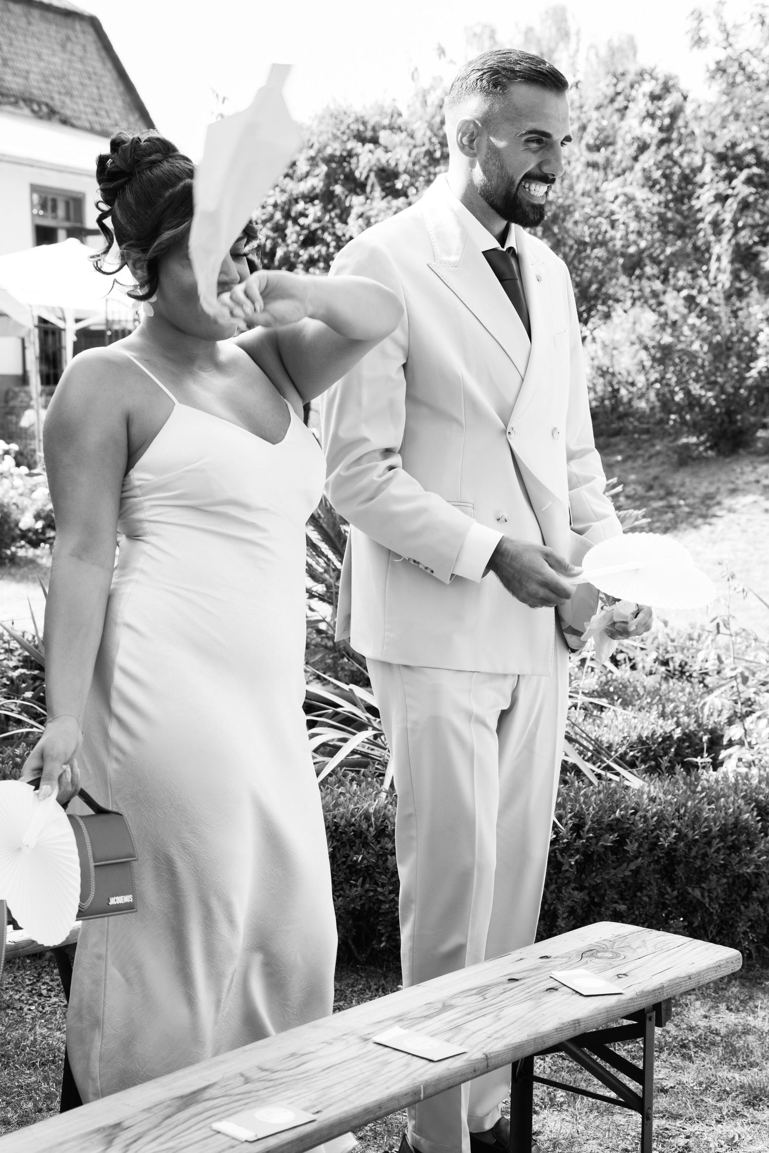 Bride and groom in white suit share emotional moment at outdoor wedding ceremony.