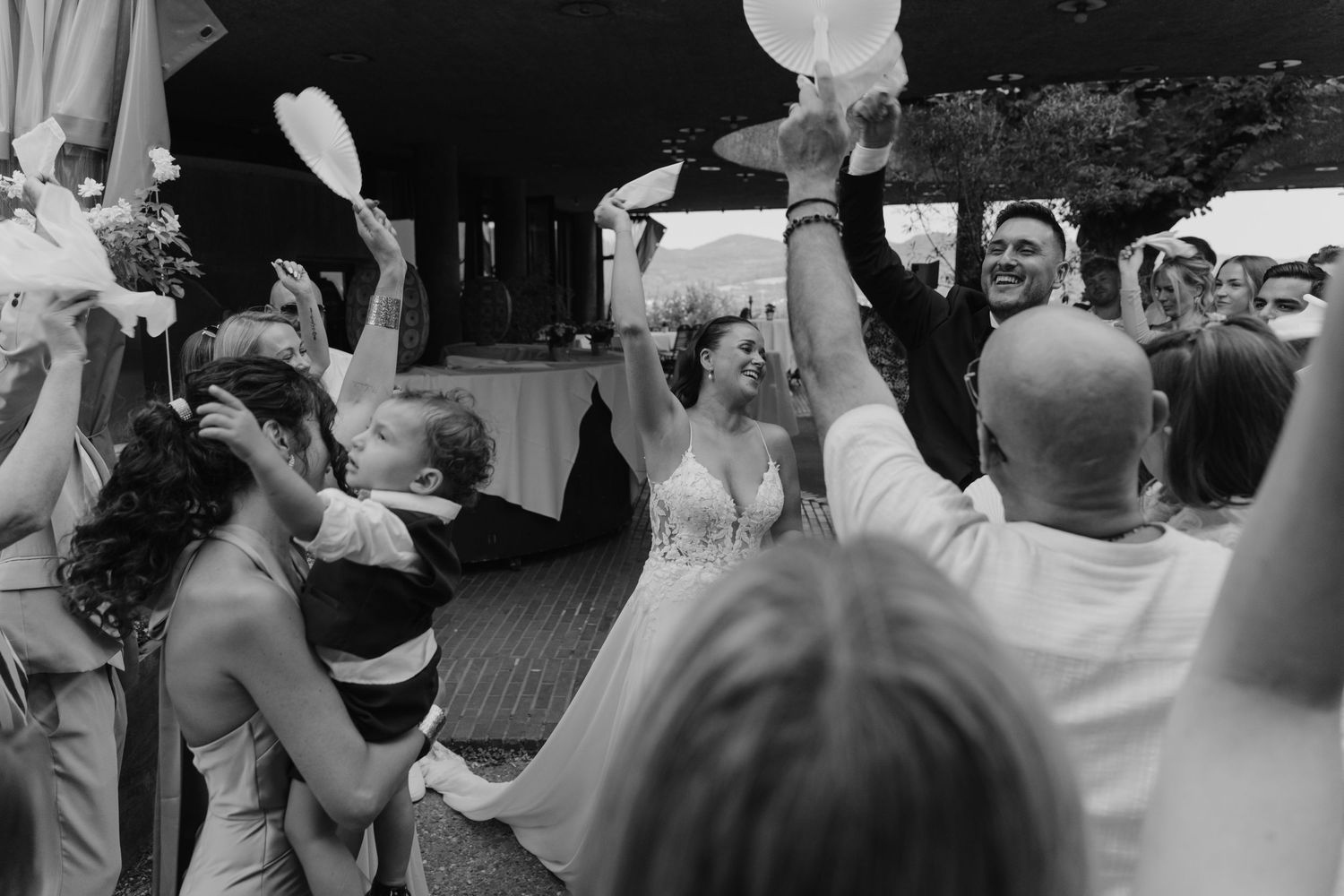 Joyful bride and groom celebrating with guests raising white items at a lively wedding reception.