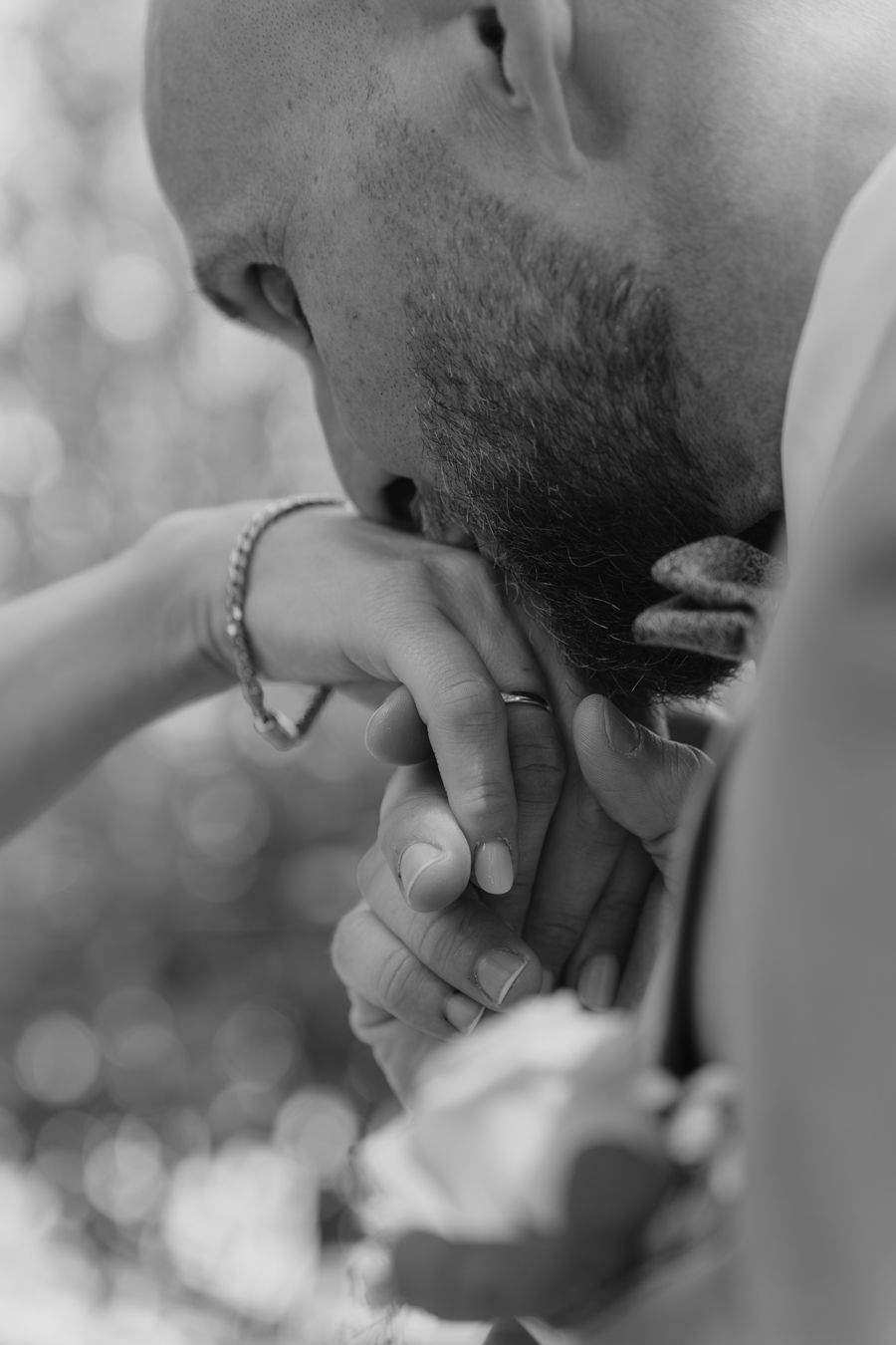 Groom tenderly kisses bride's hand in close-up black and white wedding photo.