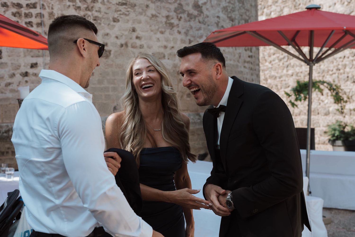 Three wedding guests laughing and socializing together at an outdoor wedding reception venue.