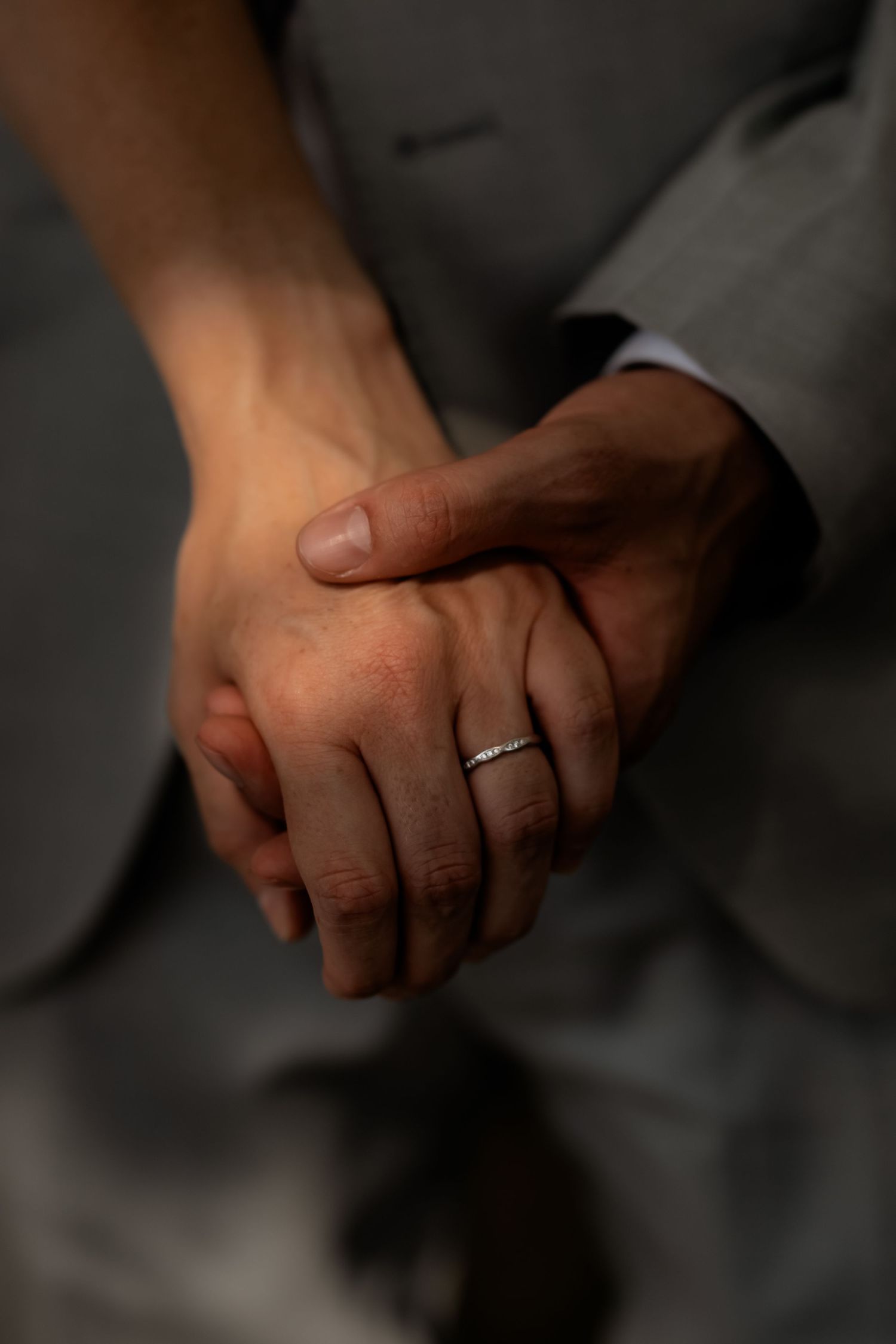 Close-up of newlyweds holding hands with wedding ring in soft dramatic lighting.