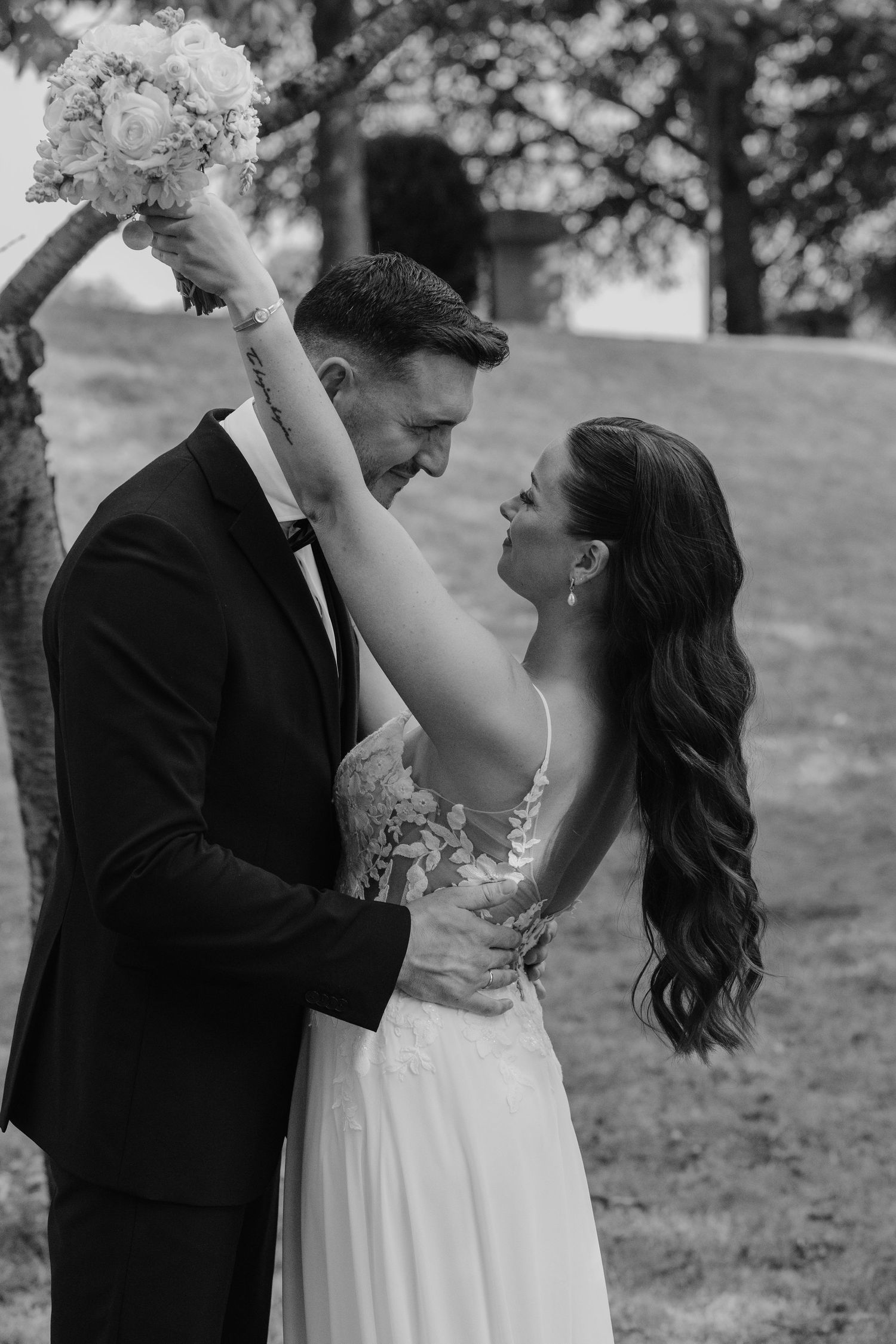 Bride raises bouquet while embracing groom, sharing a joyful moment in black and white wedding portrait.