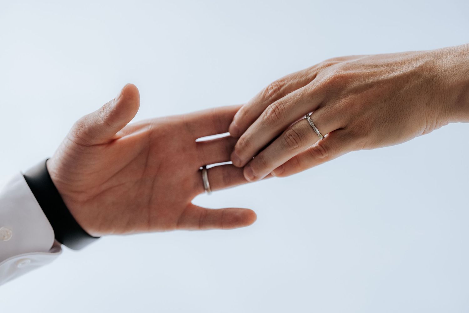Bride and groom touching hands with wedding rings on white background.