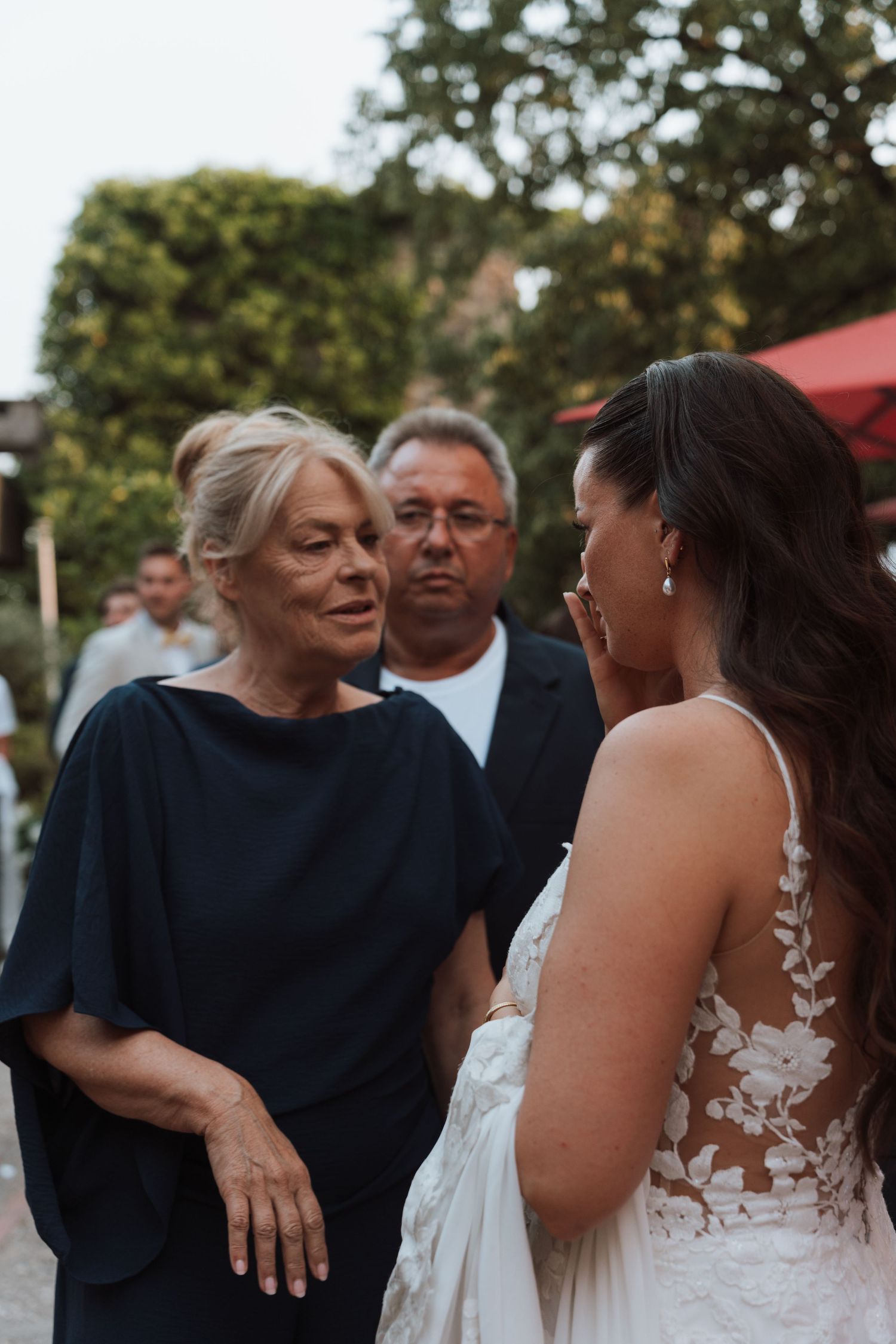Bride in lace gown having an emotional conversation with an older woman at outdoor wedding reception.