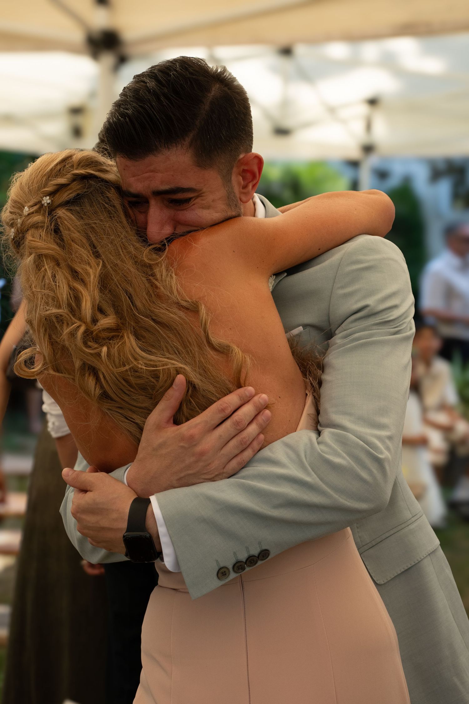 Emotional wedding moment as bride and groom share heartfelt hug under reception tent.