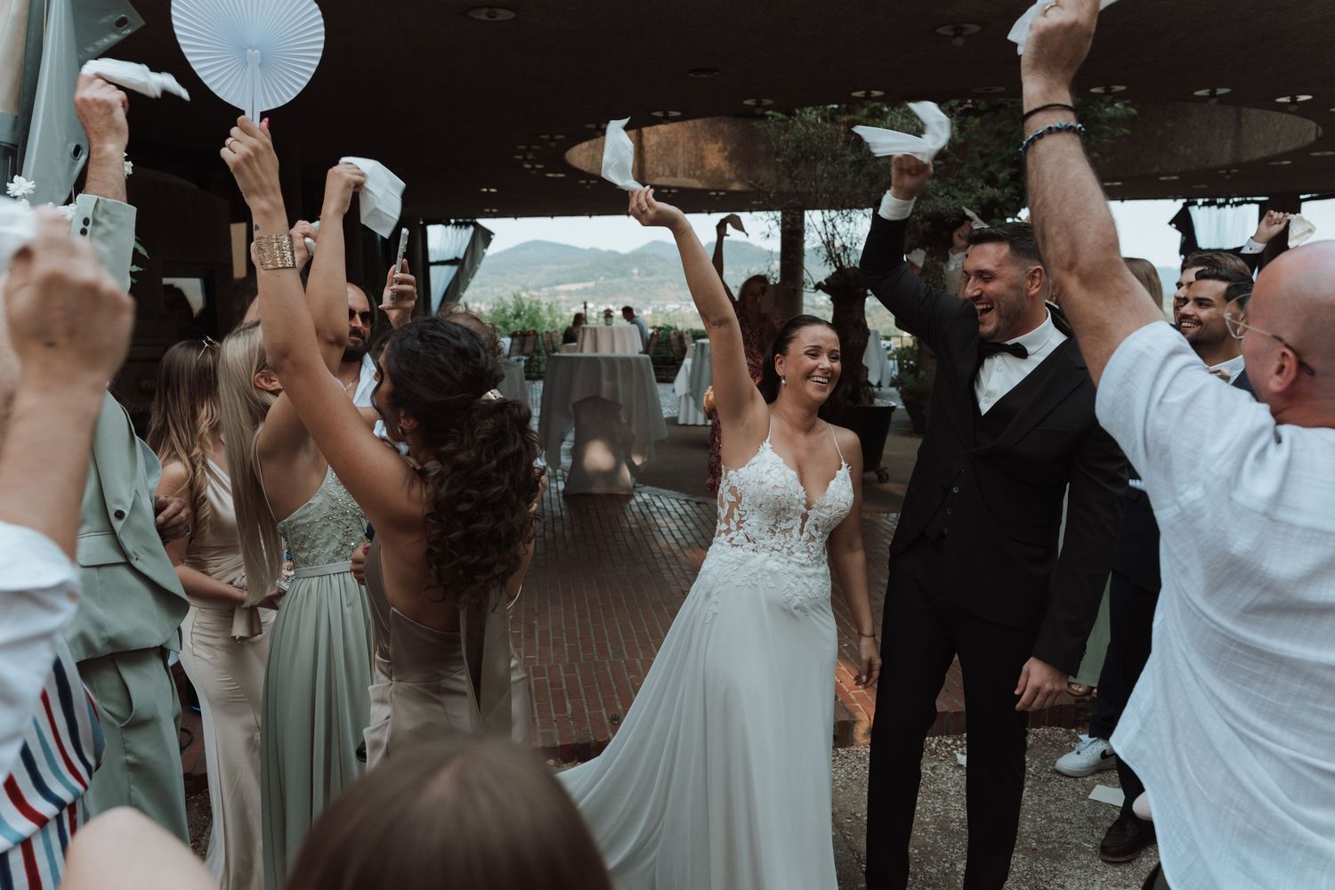 Bride and groom celebrating with guests waving white handkerchiefs at outdoor wedding reception.