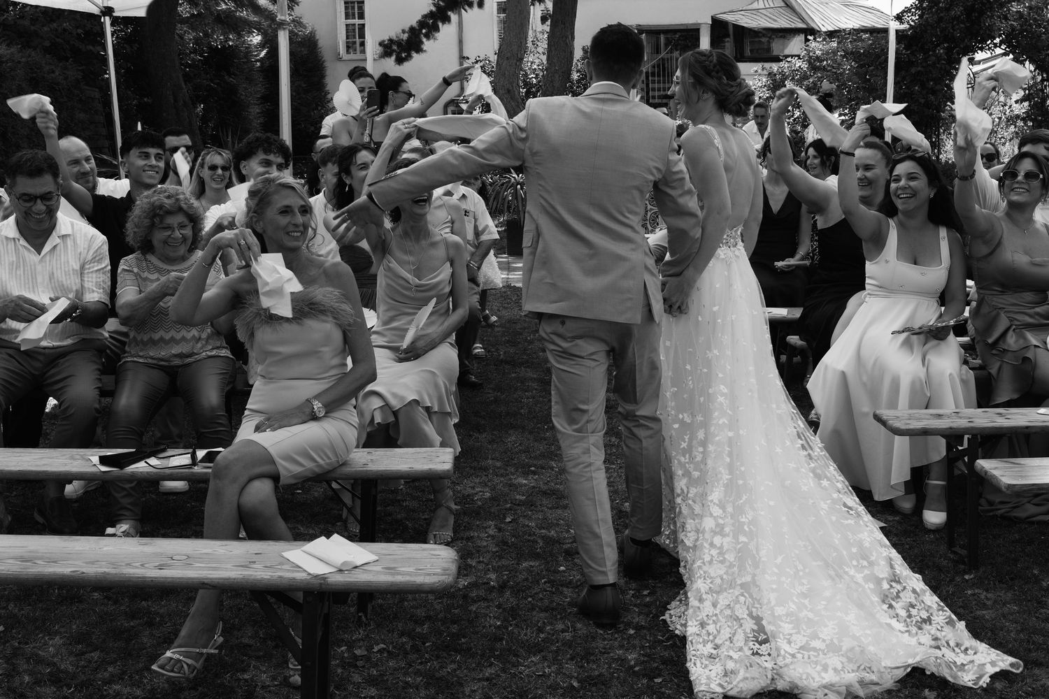 Bride and groom walk through cheering guests at outdoor wedding ceremony in black and white.