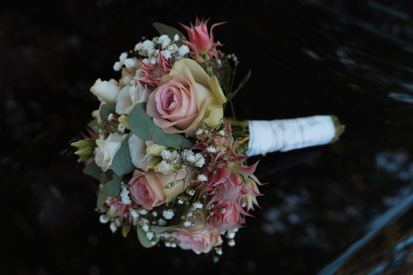 Bridal bouquet with pink roses, baby's breath, and greenery on dark background.