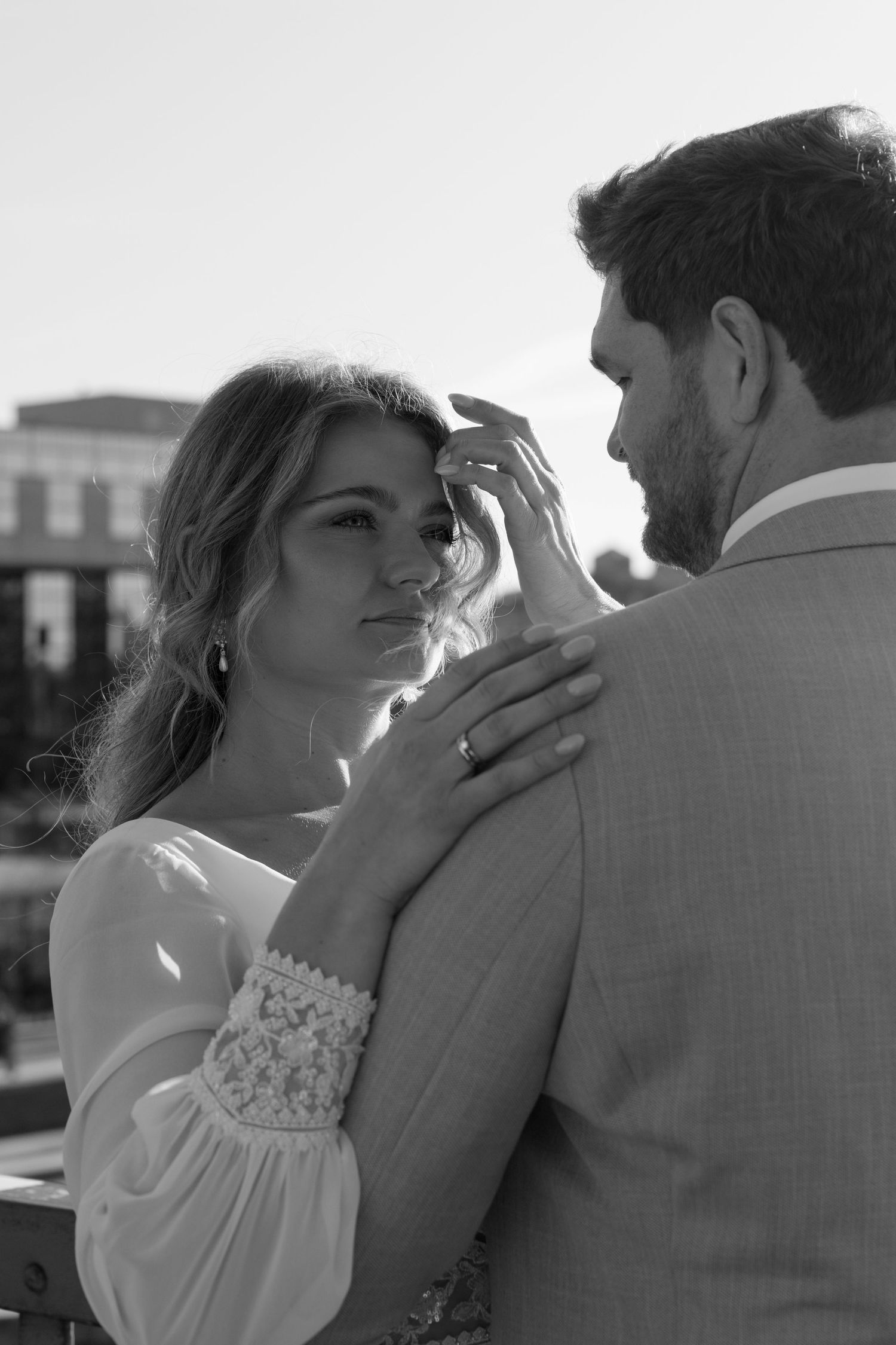 Black and white close-up of bride touching grooms face tenderly, wearing wedding ring and lace sleeve dress.