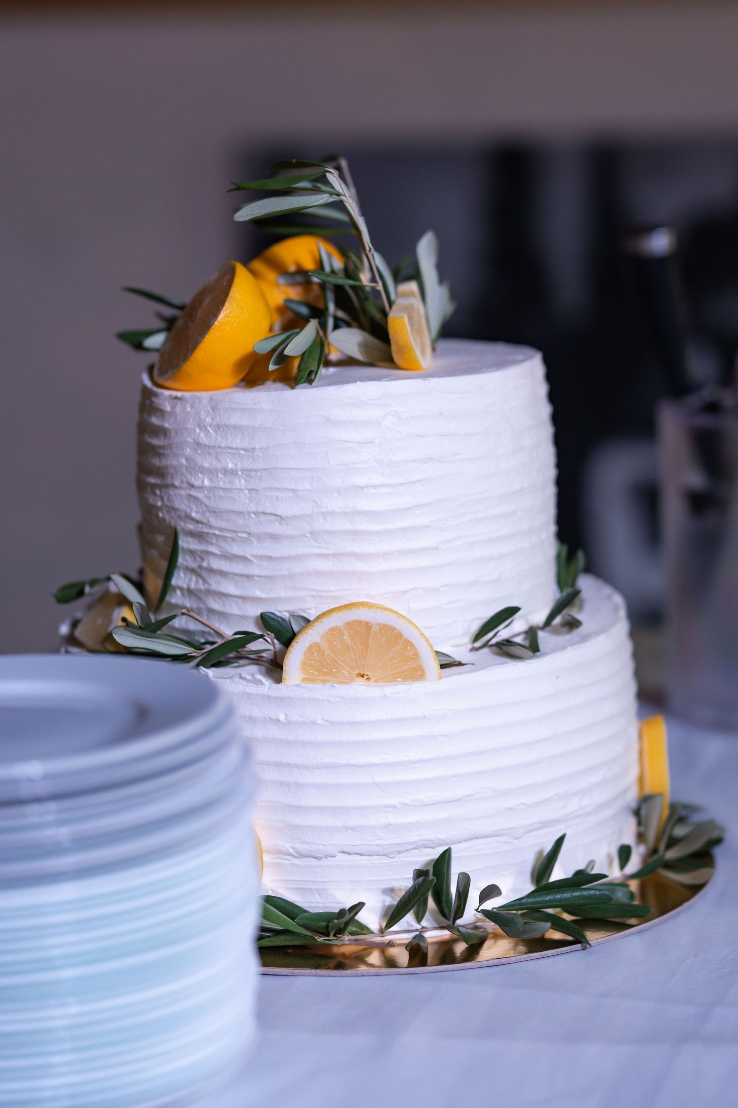 Two-tier white wedding cake decorated with lemon slices and olive branches.