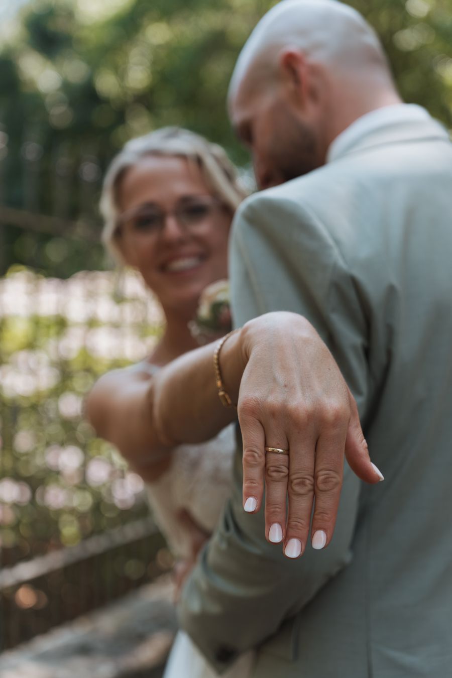 Bride shows off wedding ring with eye tattoo on hand while embracing groom.