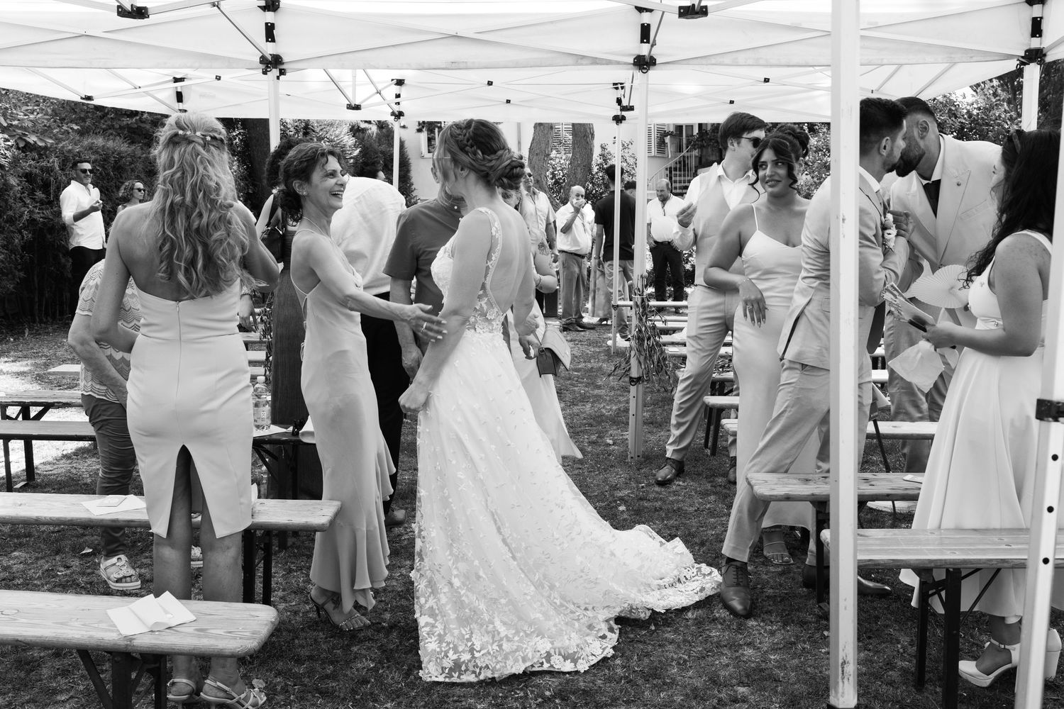 Bride in lace gown surrounded by bridesmaids in white dresses at outdoor wedding reception.