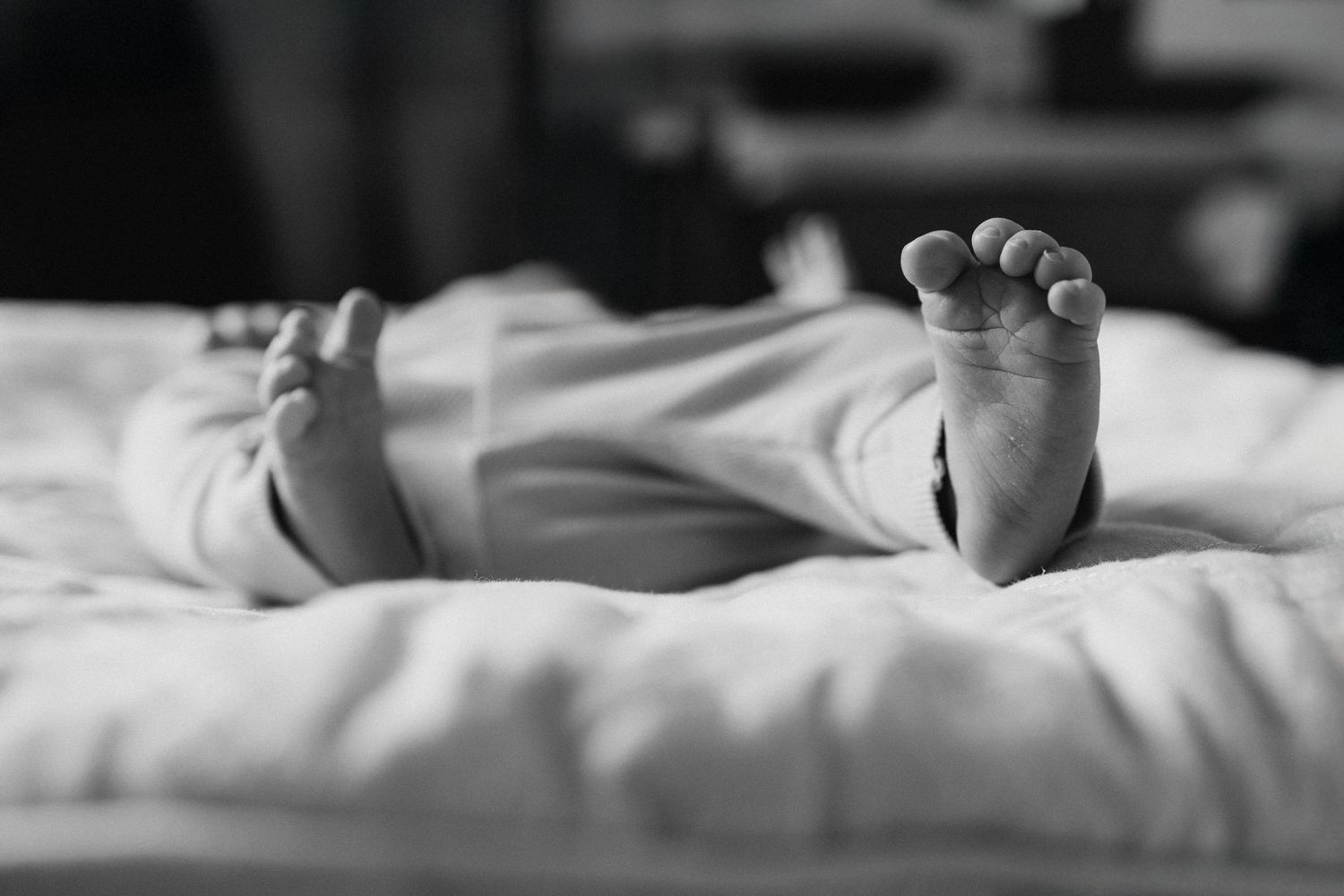 Black and white photo of newborn baby feet peeking out from white blankets on a bed.