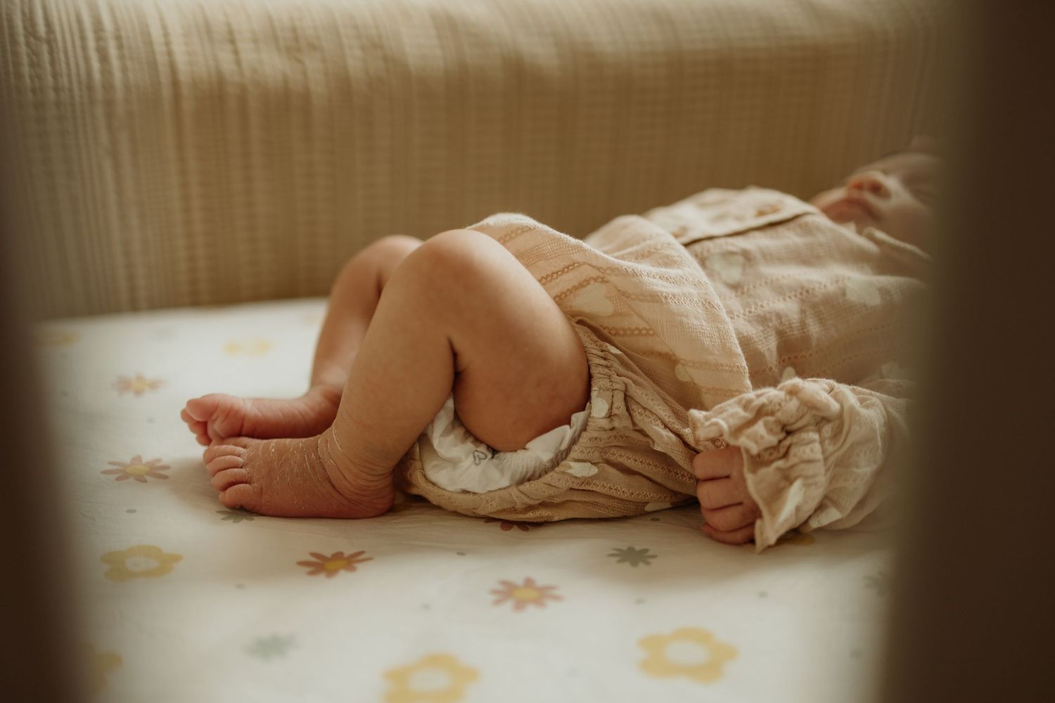 Sleeping baby lying on a floral crib mattress wearing a cream romper.