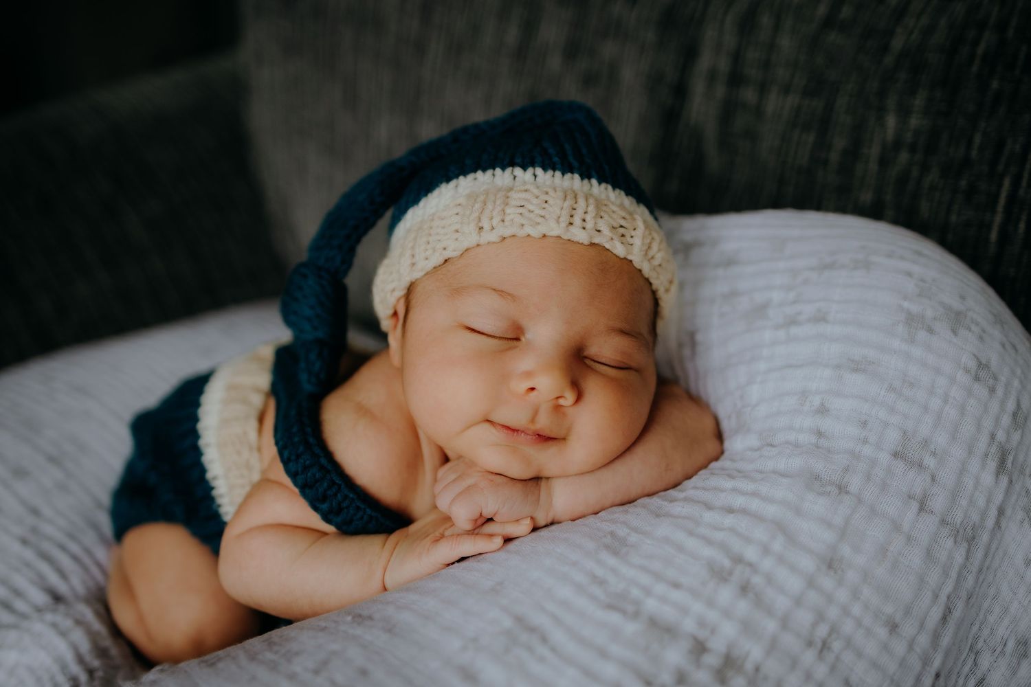 Sleeping newborn baby wearing knit blue hat and outfit posed on soft blanket.