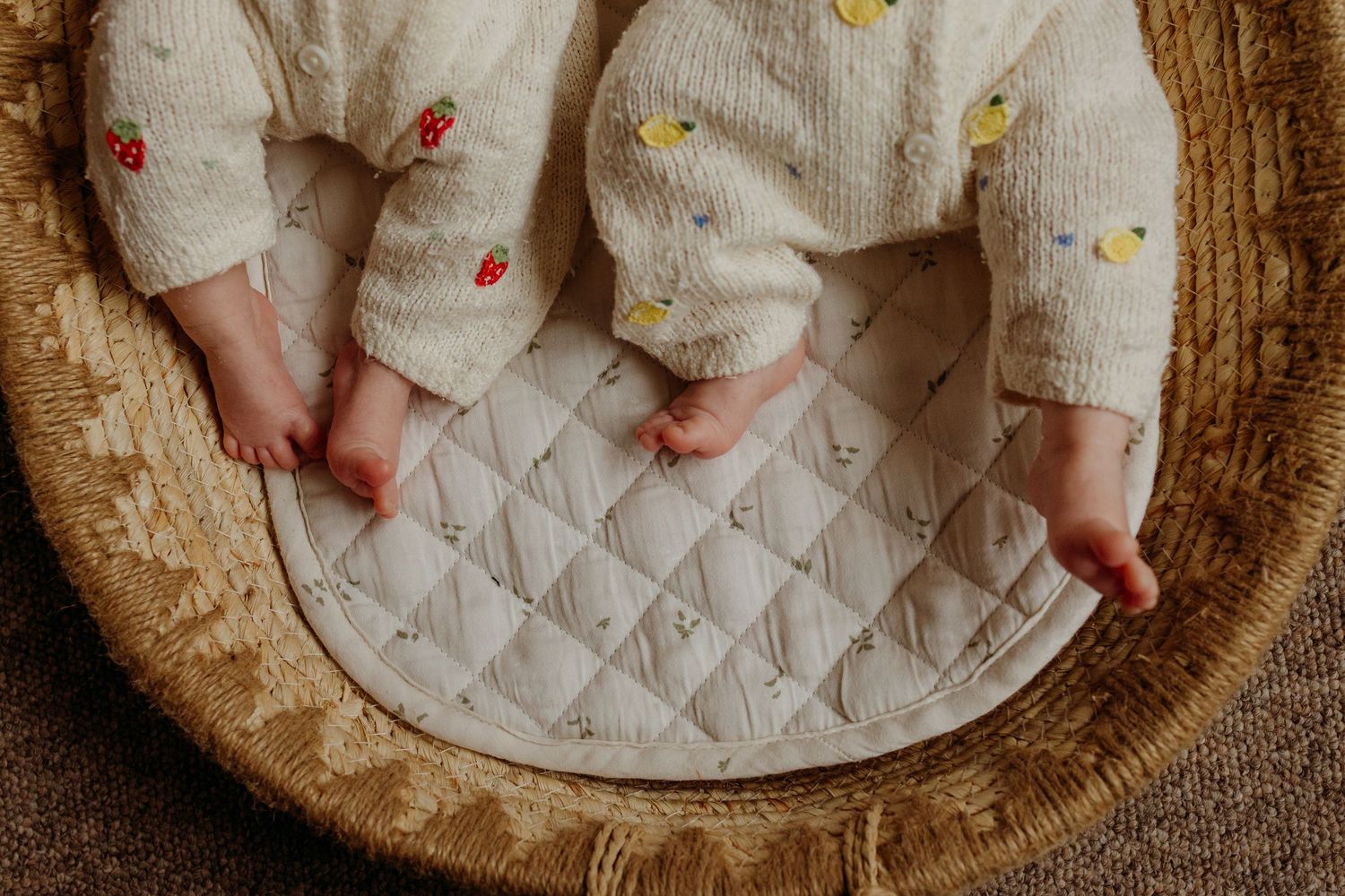 Close-up of twin babies feet in embroidered white rompers in a basket.
