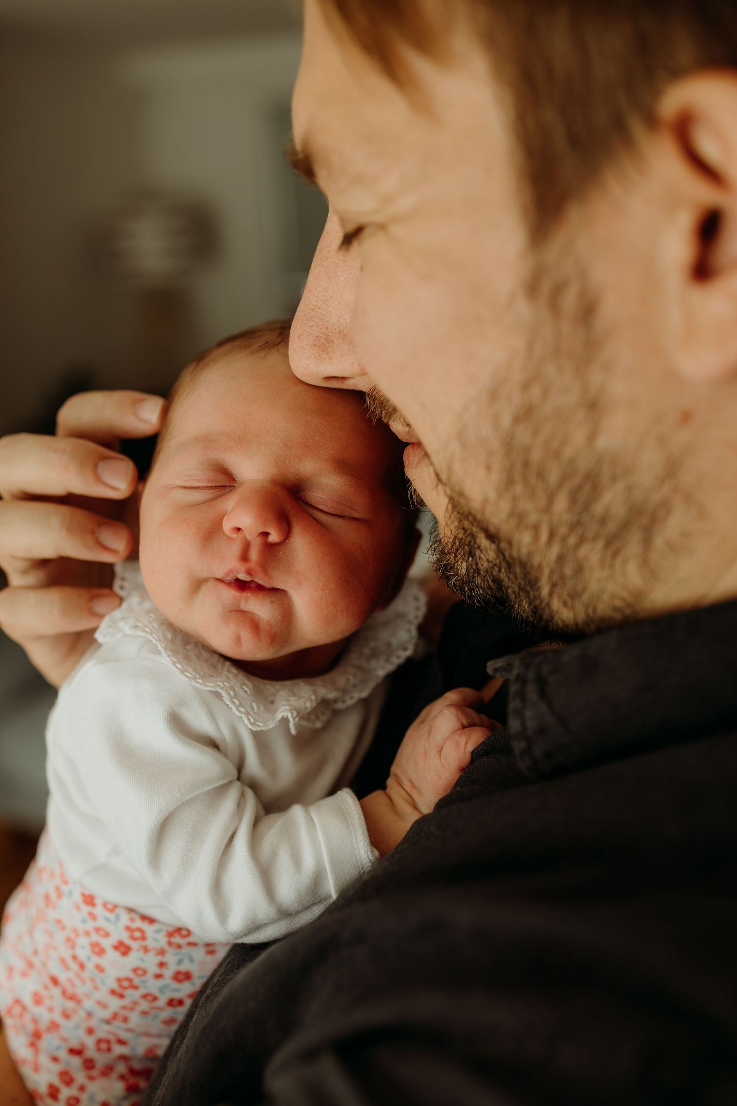 Bearded father gently nuzzling his sleeping newborn baby girl.