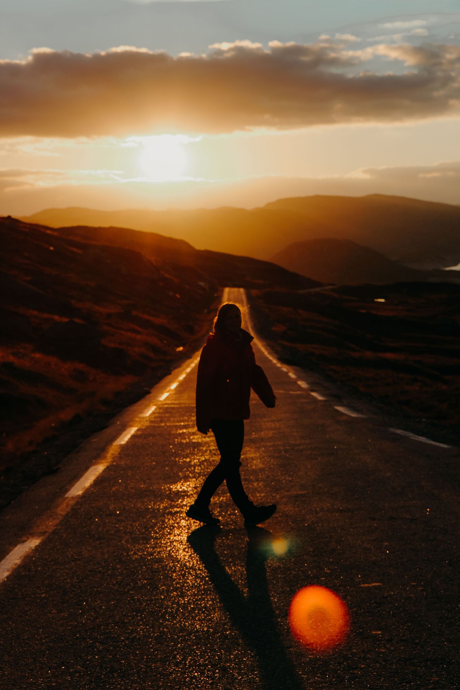 Silhouette of woman walking on empty road during golden sunset in mountain landscape.